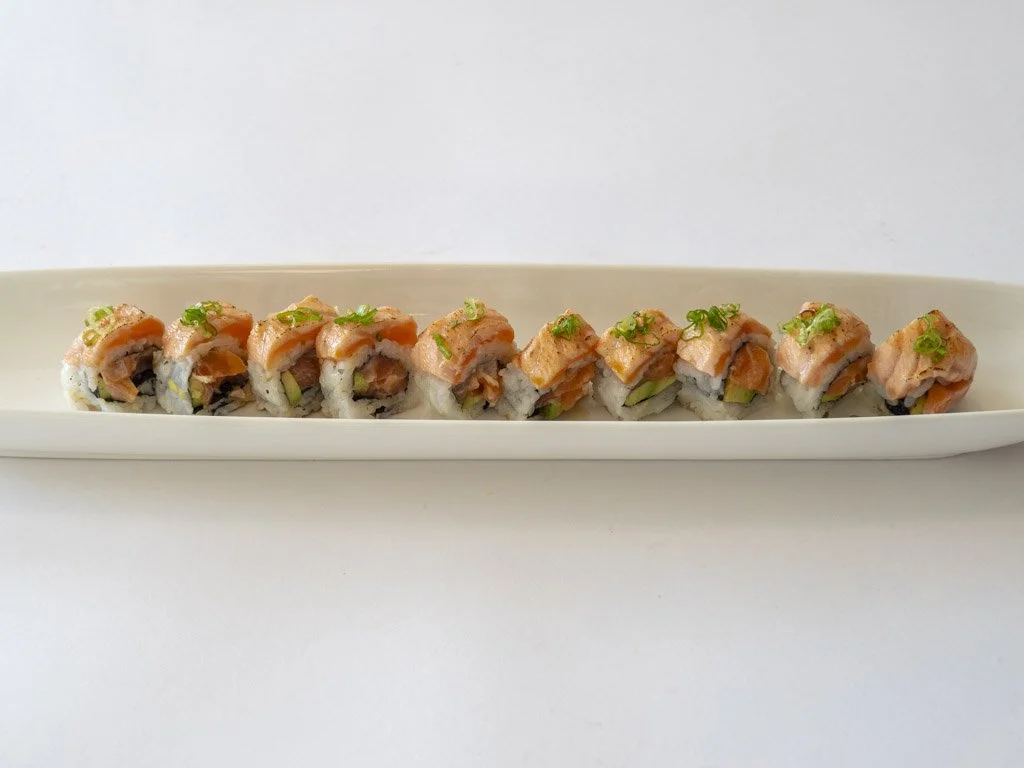 Sushi roll with salmon, avocado, and rice on a white platter.