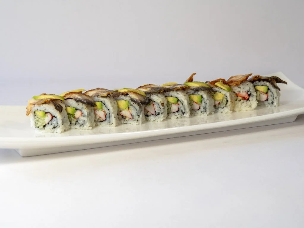 A long white platter with sushi rolls, each containing rice, cucumber, crab meat, and topped with fish.