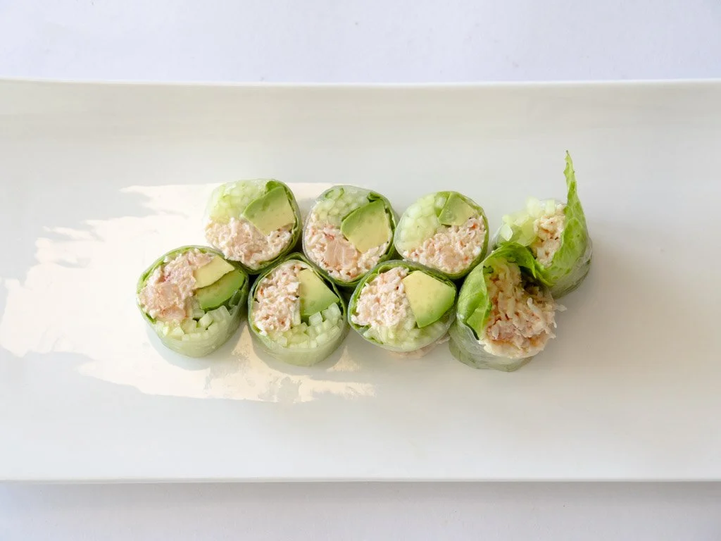 Seven cucumber sushi rolls filled with salmon, avocado, and rice, arranged on a white rectangular plate.