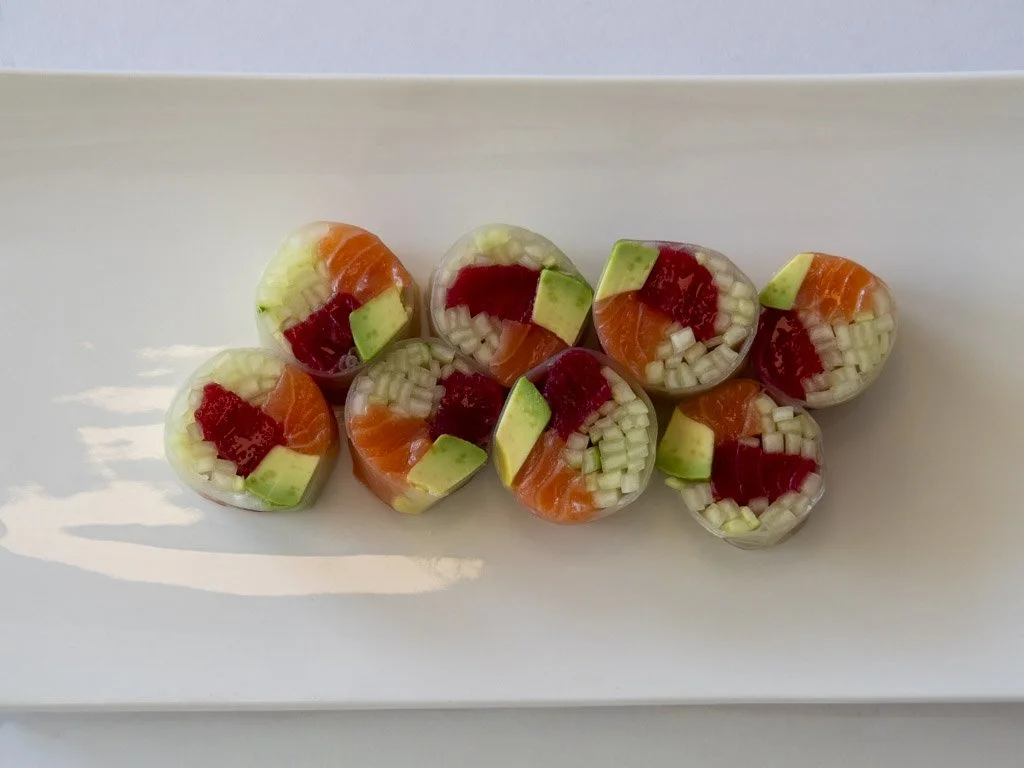 Eight sushi rolls with rice, salmon, cucumber, and red fish, arranged on a white plate.