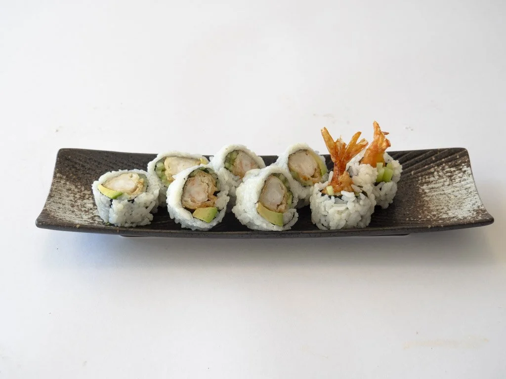 Sushi rolls with shrimp, avocado, and rice on a black rectangular plate