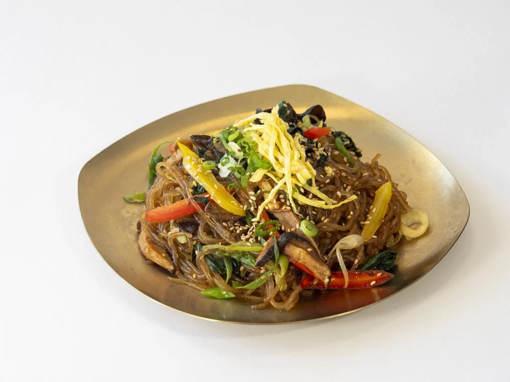 A plate of stir-fried noodles with vegetables topped with shredded cheese and sesame seeds