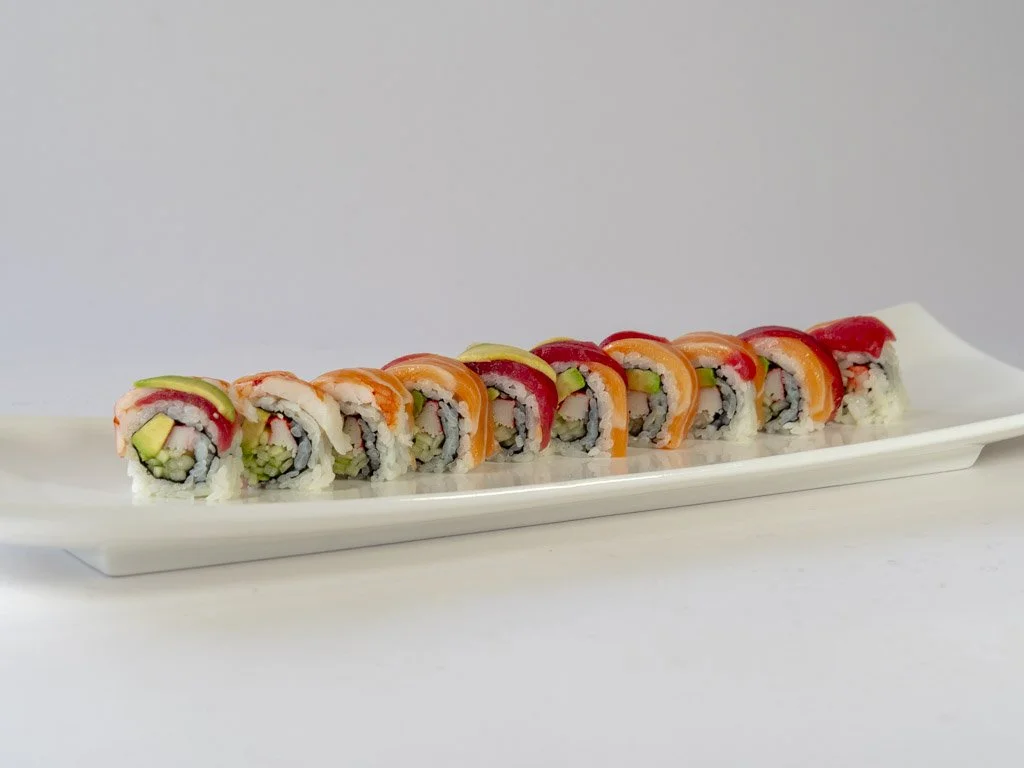 Assorted sushi rolls arranged on a white rectangular plate, with slices of cucumber, avocado, and fish visible inside.