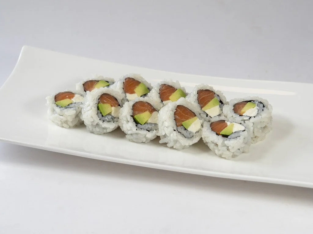 A white rectangular plate with eight sushi rolls, containing salmon, avocado, and rice, arranged in a single row.