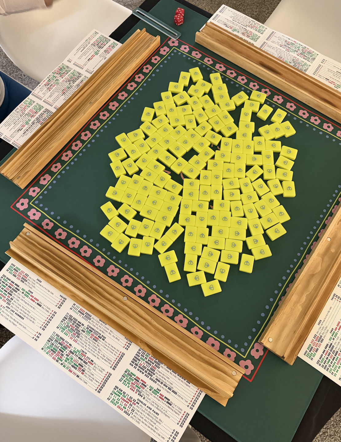 A green wooden board with pink flower borders, yellow tiles with blue numbers, and betting sheets around the edges, used for a game of bingo.
