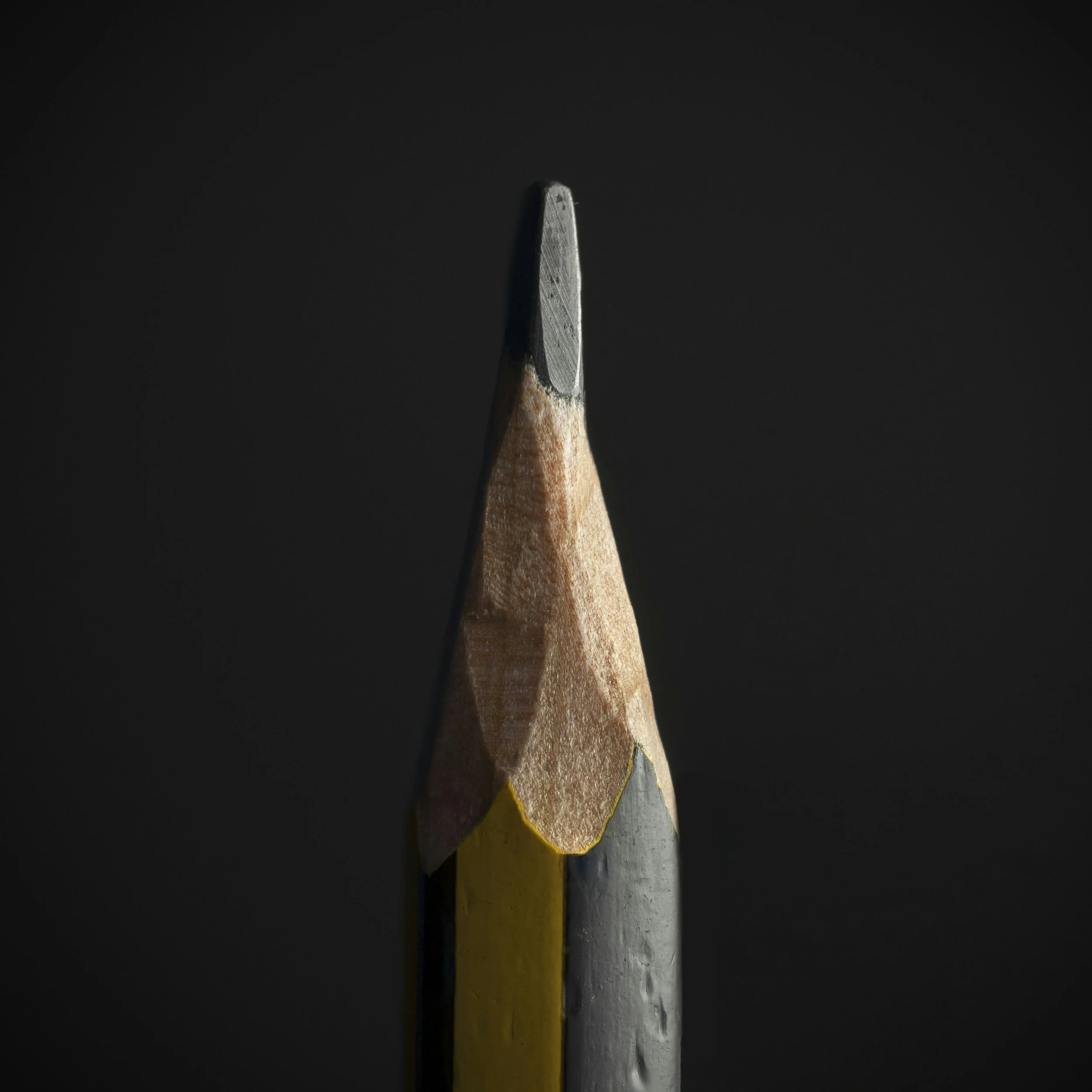 Close-up of a pencil standing upright on a dark background.