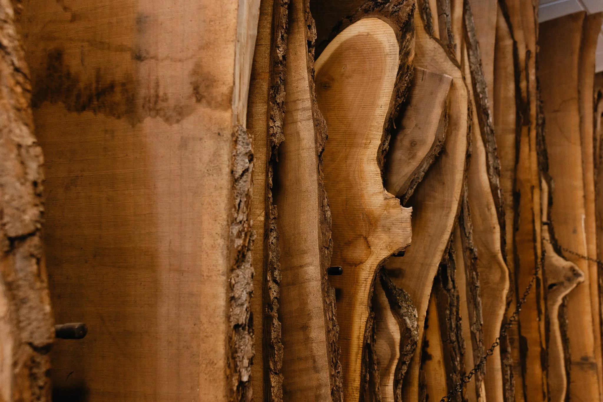 Stacked raw wood slabs, with rough bark on some pieces and smooth, sanded surfaces on others, arranged vertically.