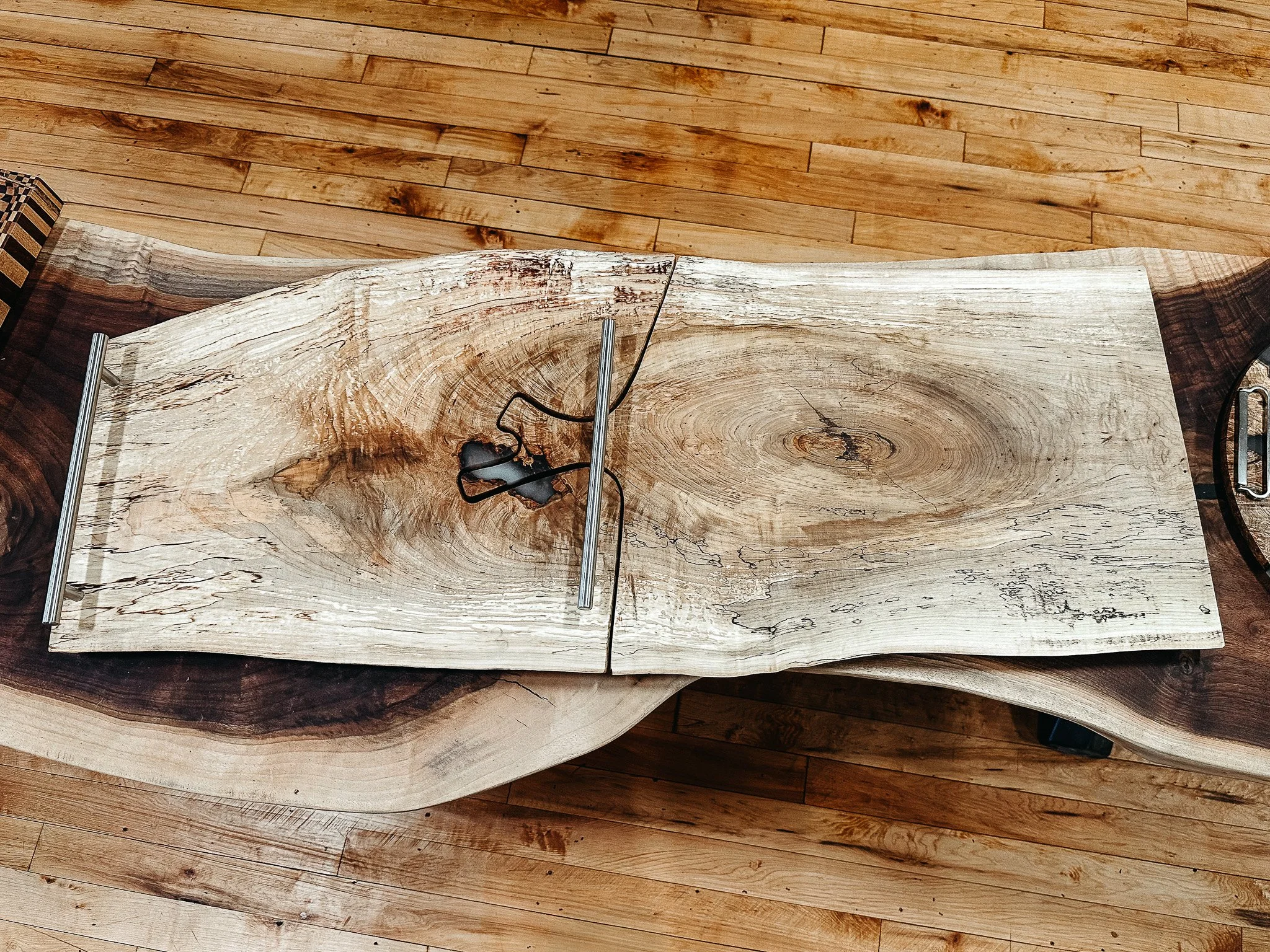 Close-up of a rustic, split log wood table with black cord and metal stand on top, and a wood floor background.