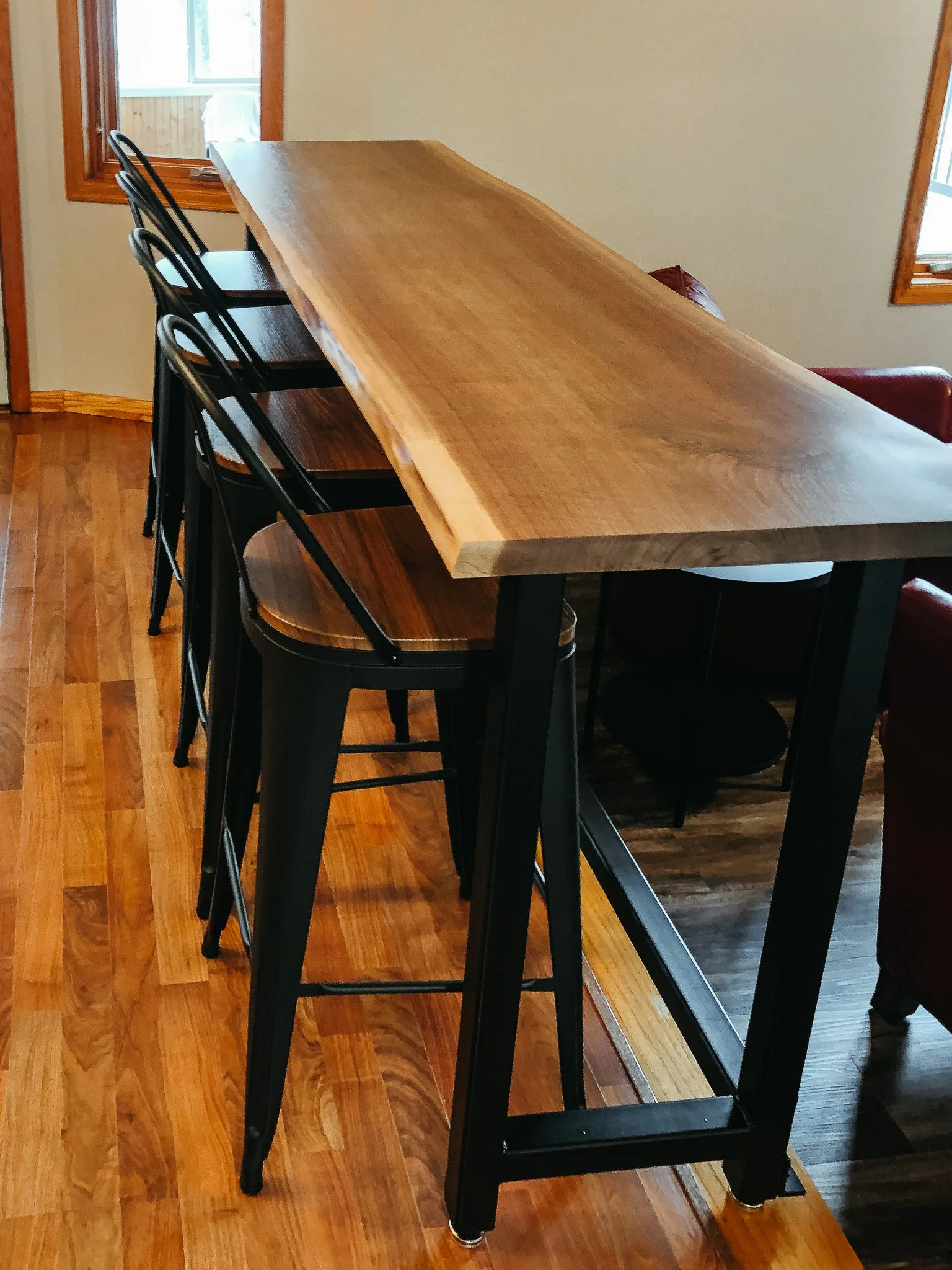 A wooden countertop or table with black metal legs in a room with wooden floors and two windows.