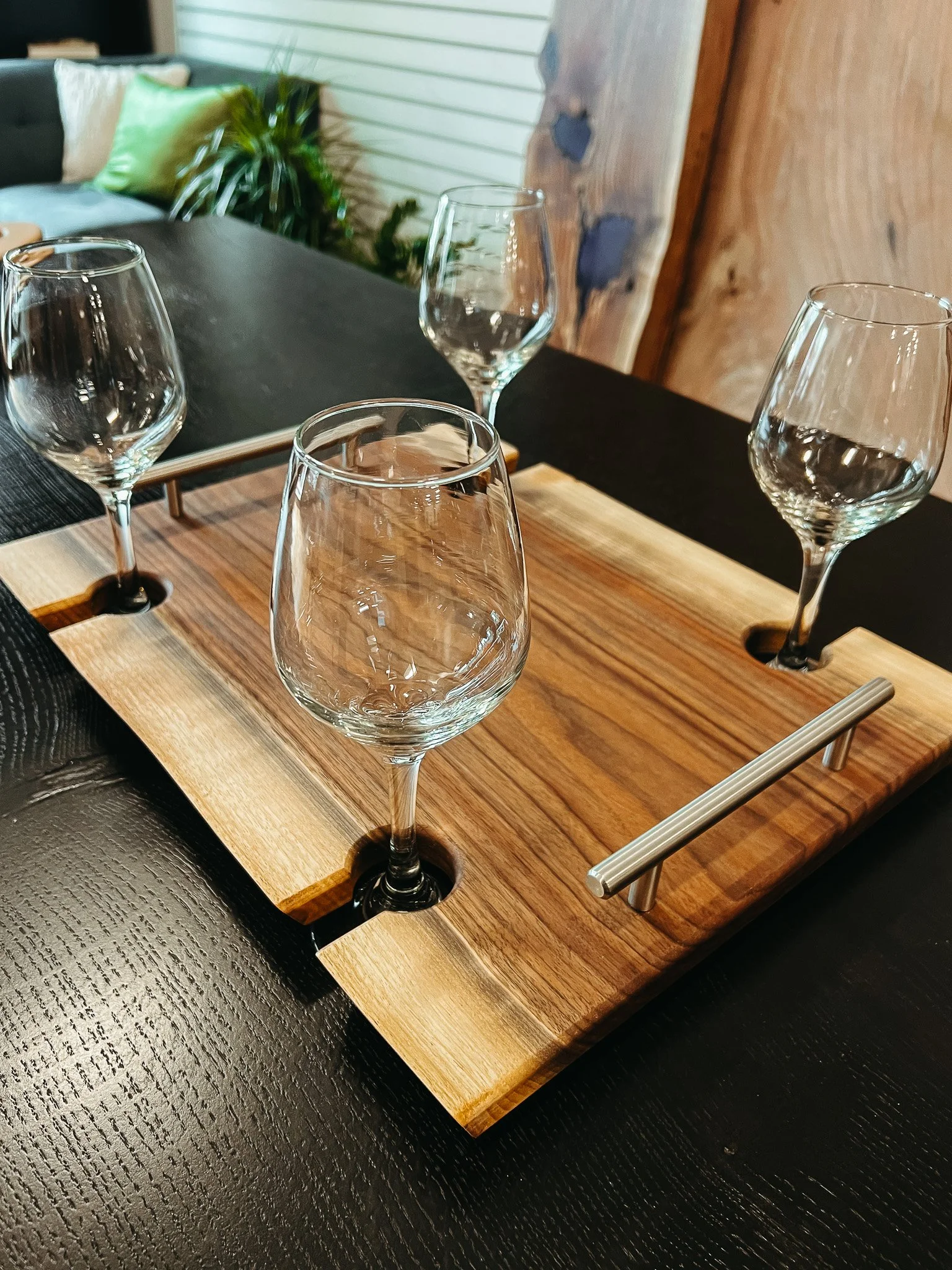 A wooden whiskey tasting flight with four empty wine glasses placed on a black table. The flight has a metal handle for carrying.