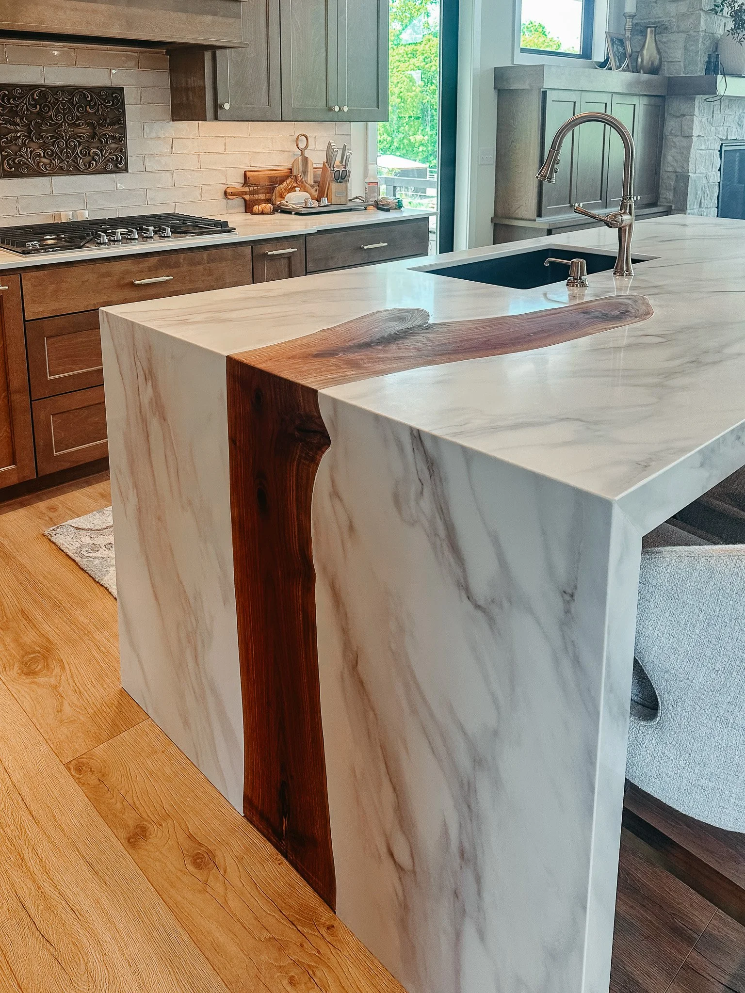 Modern kitchen with a marble island, gray cabinets, and a sliding door leading outside, decorated with vases and framed photos.