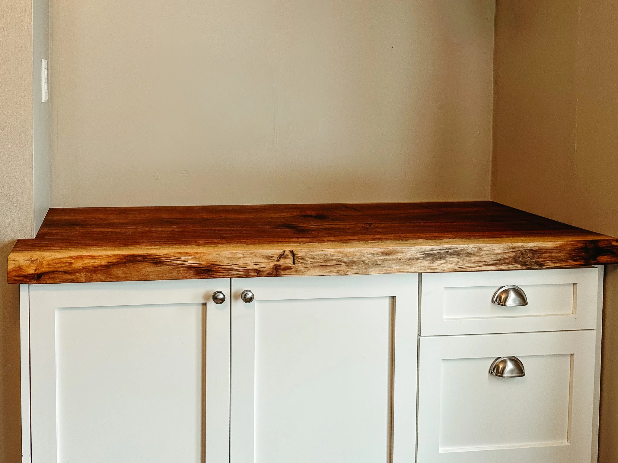 A white kitchen cabinet with four drawers and two doors, topped with a large, thick rectangular wooden butcher block counter.