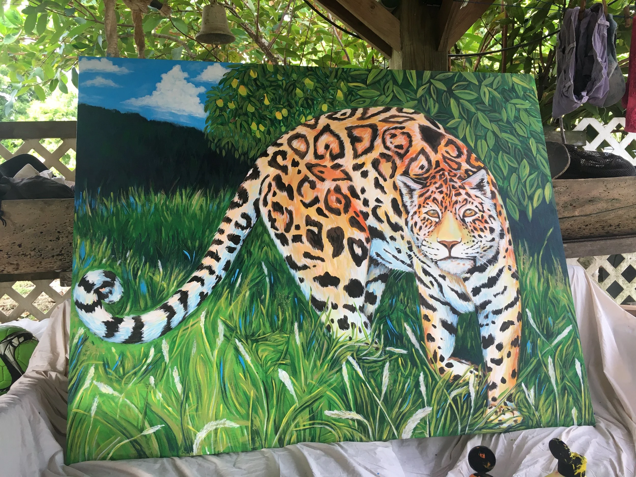 A colorful painting of a jaguar walking through a lush green jungle with trees and grass, with a blue sky and clouds in the background.
