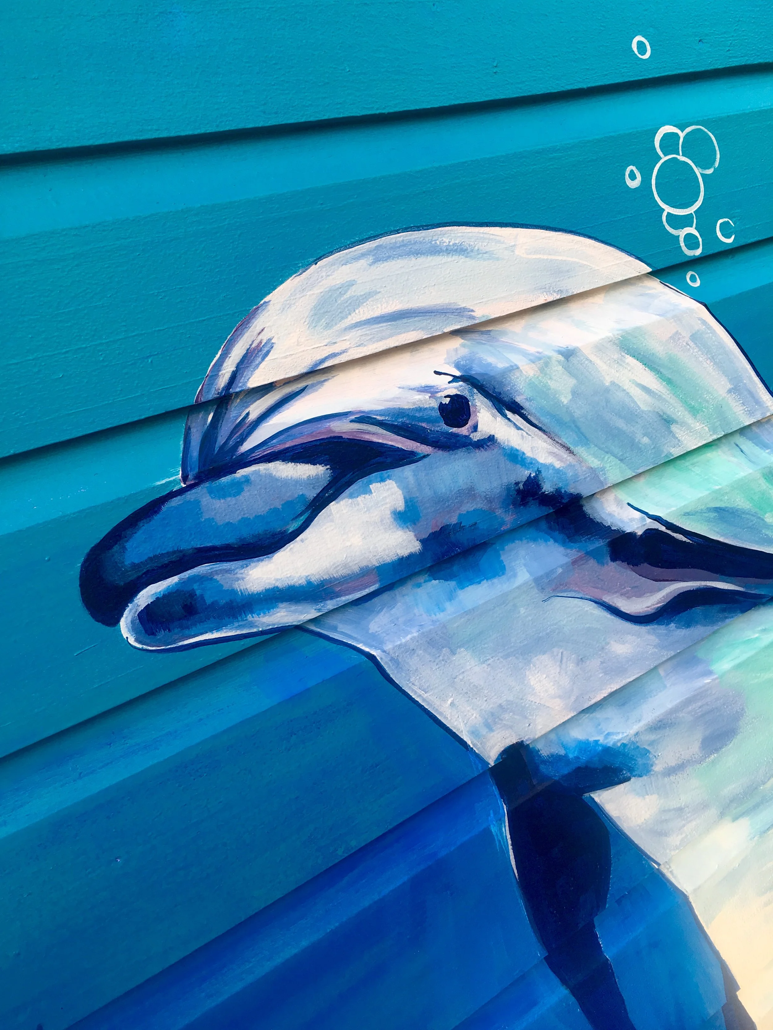 A colorful, dolphin painting on a wooden surface featuring shades of blue, white, and purple with bubble-like shapes.
