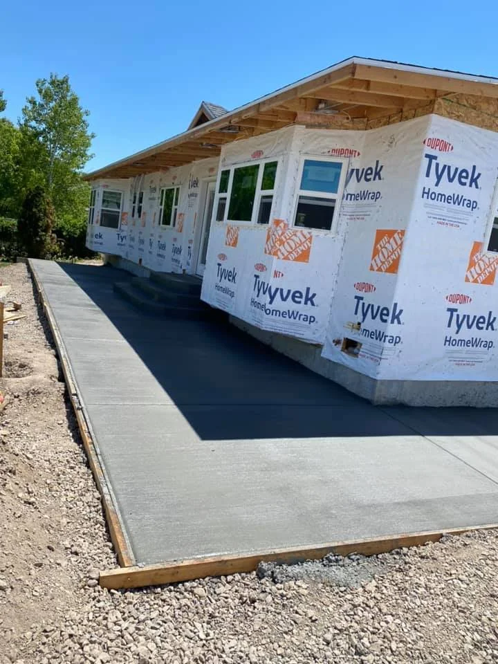 A house under construction with a freshly poured concrete sidewalk.