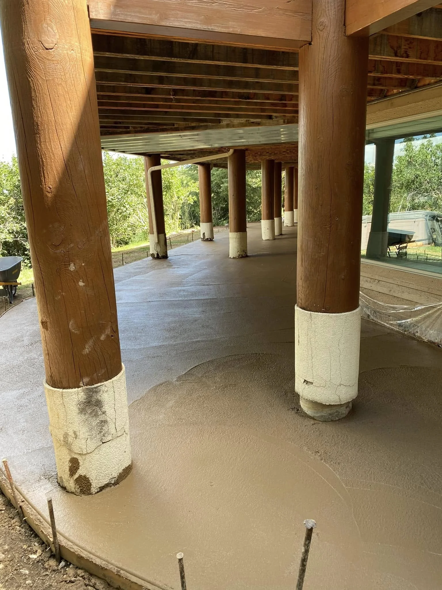 Construction site with wooden support columns and freshly poured concrete flooring.