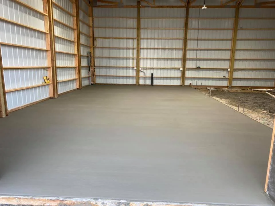 Interior of a metal barn with a freshly poured concrete floor.