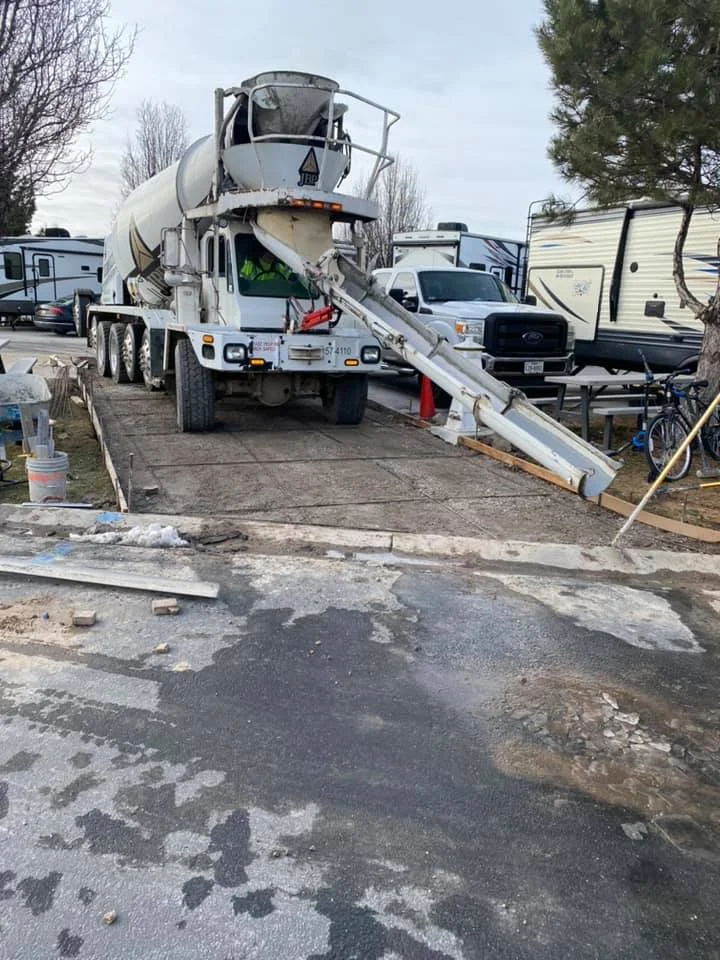 A concrete mixer truck parked on a construction site with a partially poured concrete slab and construction materials around.