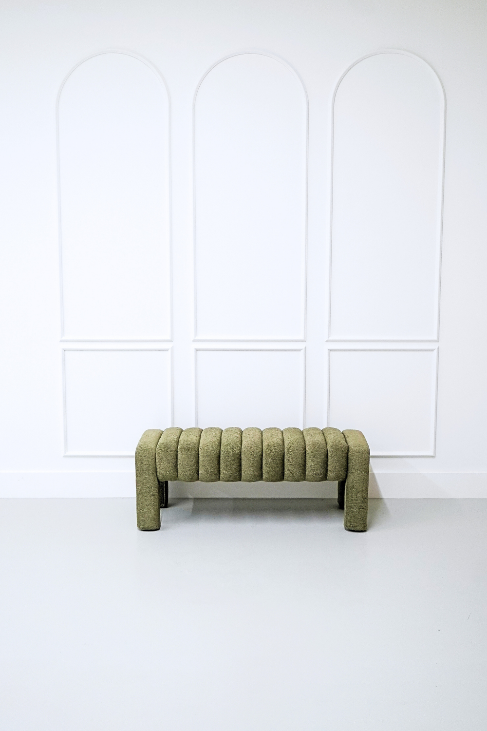 A green upholstered bench in front of a white wall with three arched panel designs.
