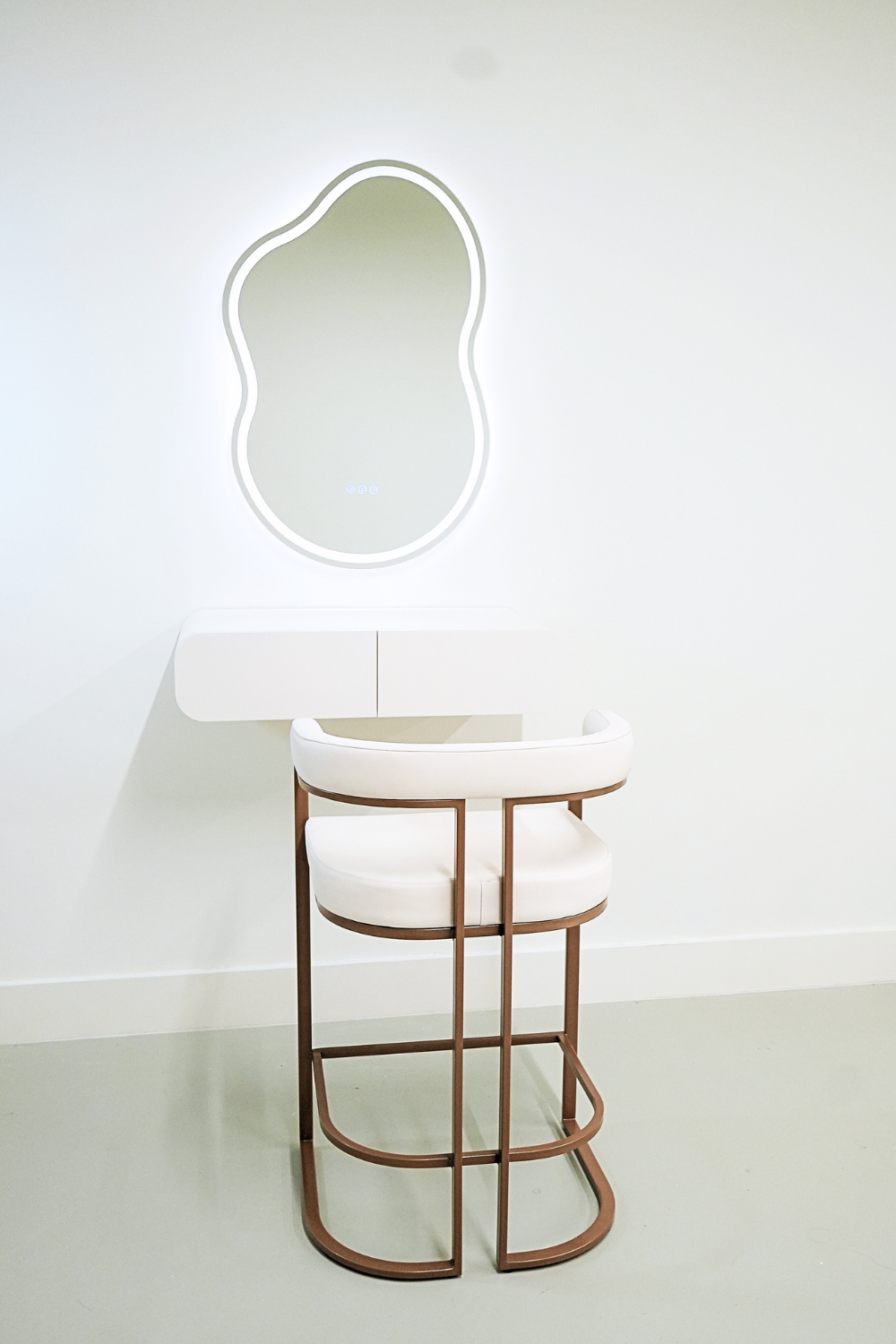 Minimalist white vanity table with a modern white chair and a wavy-shaped backlit mirror on a plain wall.
