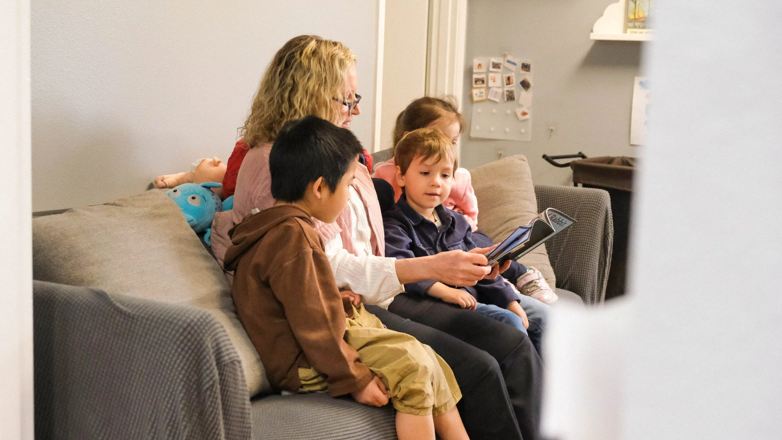 A woman and four children sitting on a couch, reading a book together in a living room.