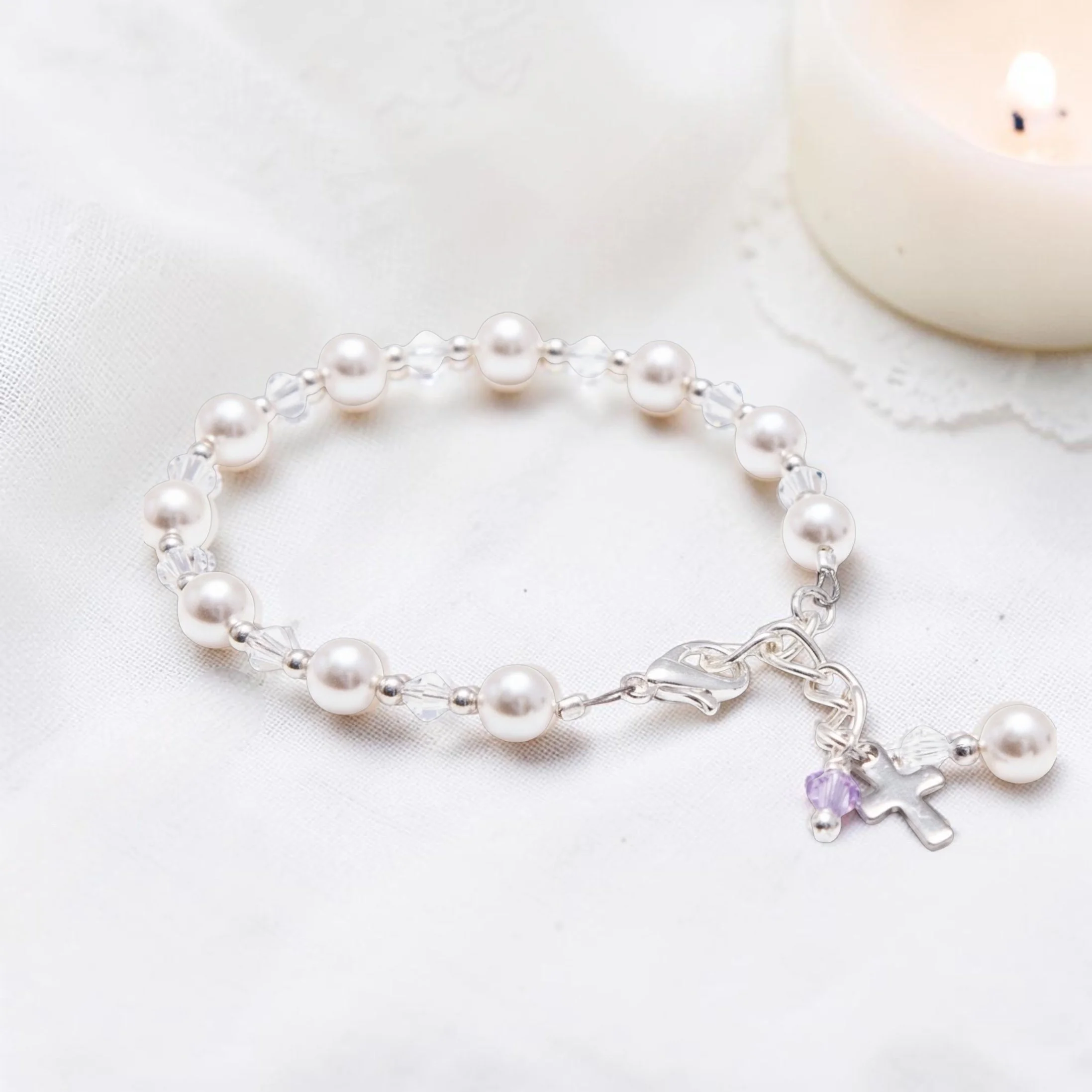 A pearl and crystal bead necklace lying on a white textured fabric, with a white spherical object in the background.
