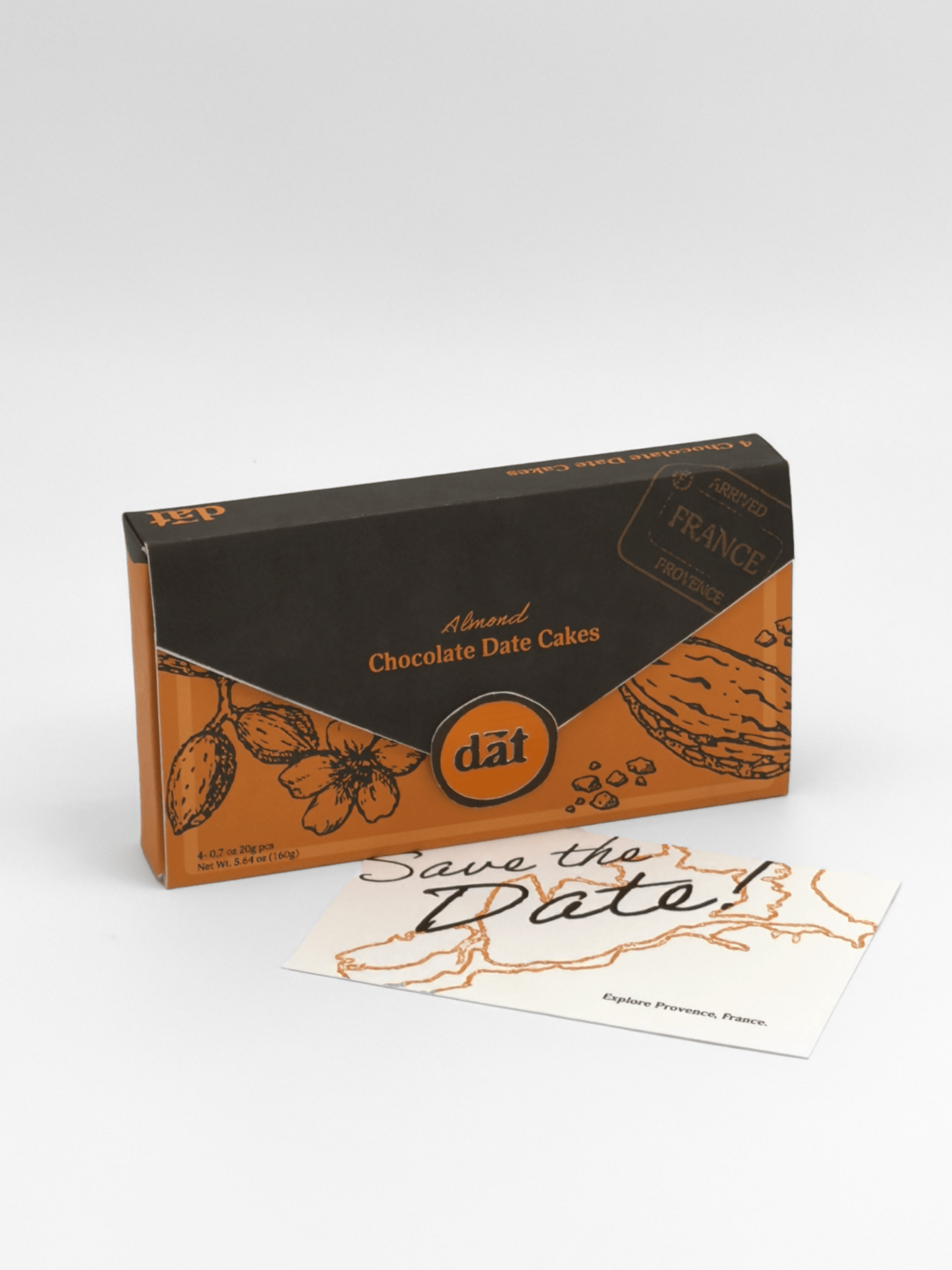Black and orange box of almond chocolate date cakes placed on a white surface, with a white note card beneath it that reads "Save the Date" and mentions Provence, France.