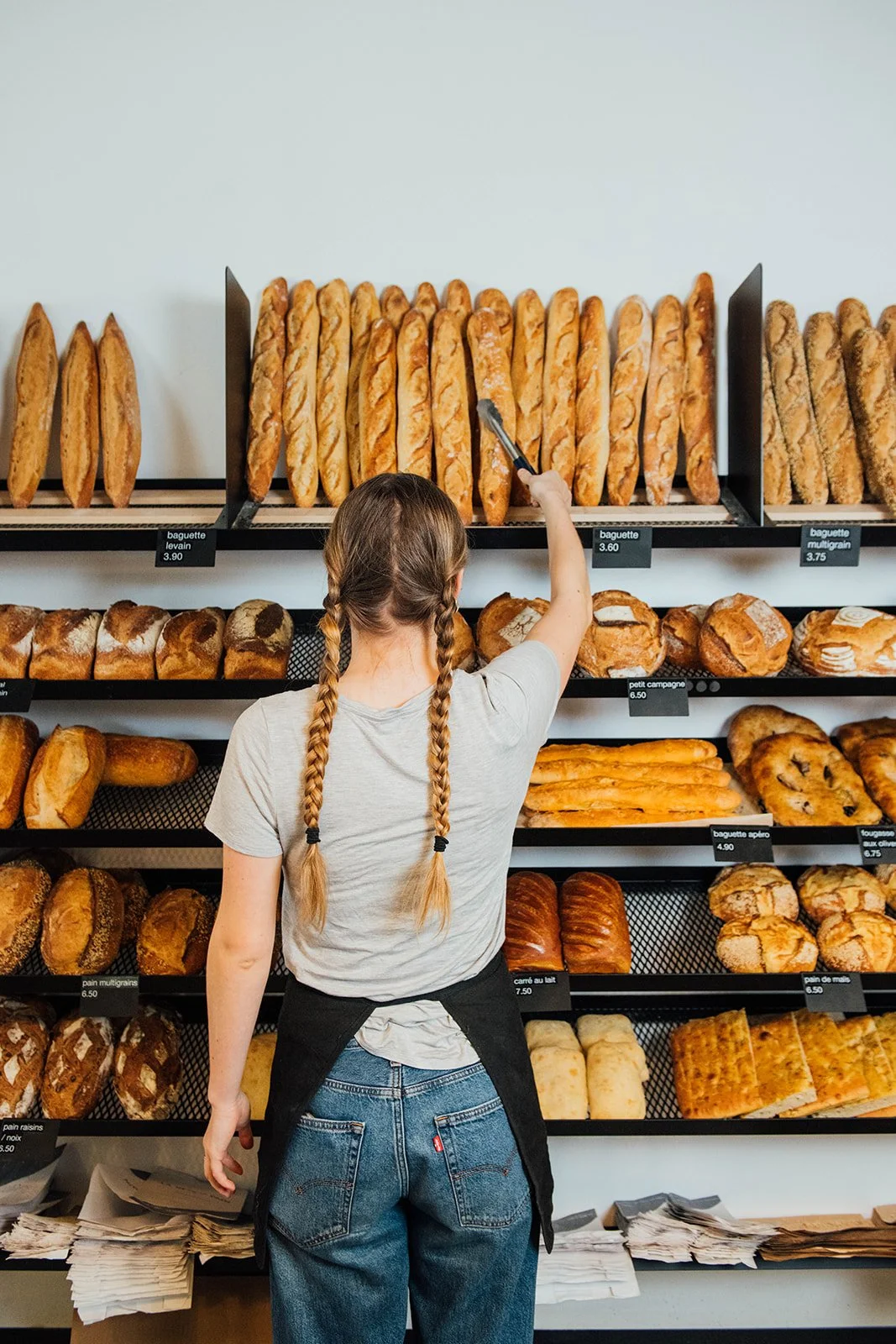 Employée de La Bête à Pain sélectionnant une baguette fraîche sur l'étagère.