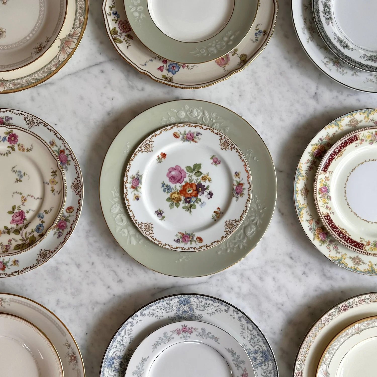 Mixed and matched vintage china in a beautifully curated 9 plate setting formation. Different floral themed dinner and salad plate combinations are designed to be a part of a elevated collection for wedding and event tableware rentals.