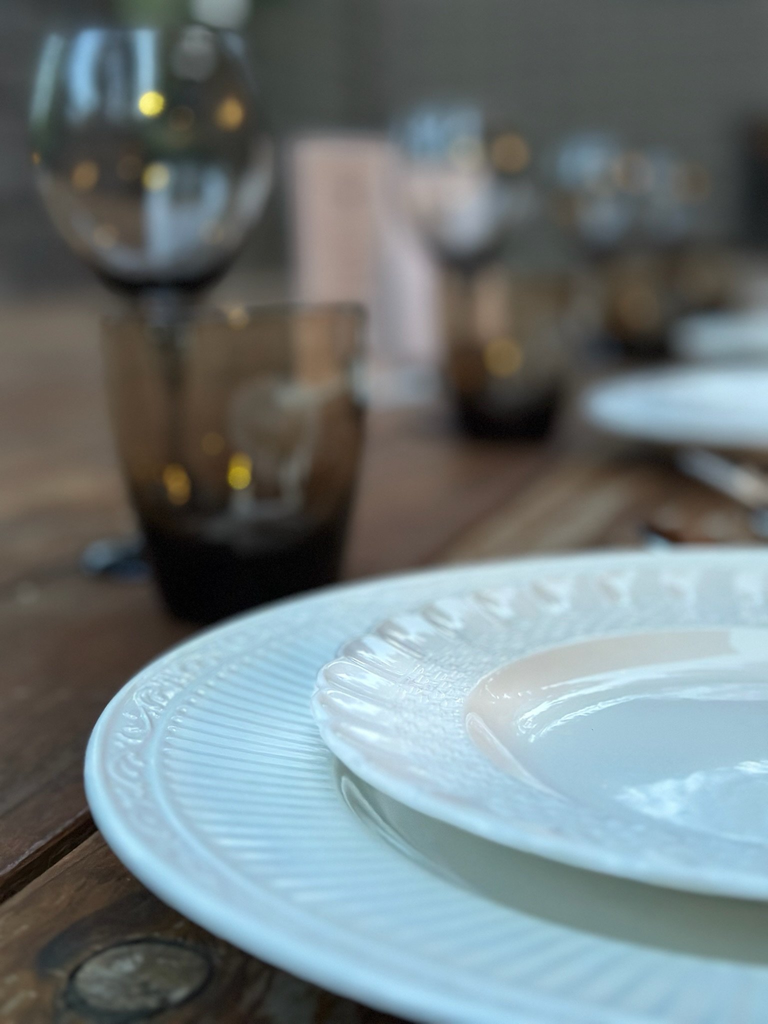 A close up photo of a dinner and salad plate setting from the curated, mix match collection, Bianca. In the background out of focus are thick, midcentury modern (MCM) water and wine glasses on a wooden table at an event.
