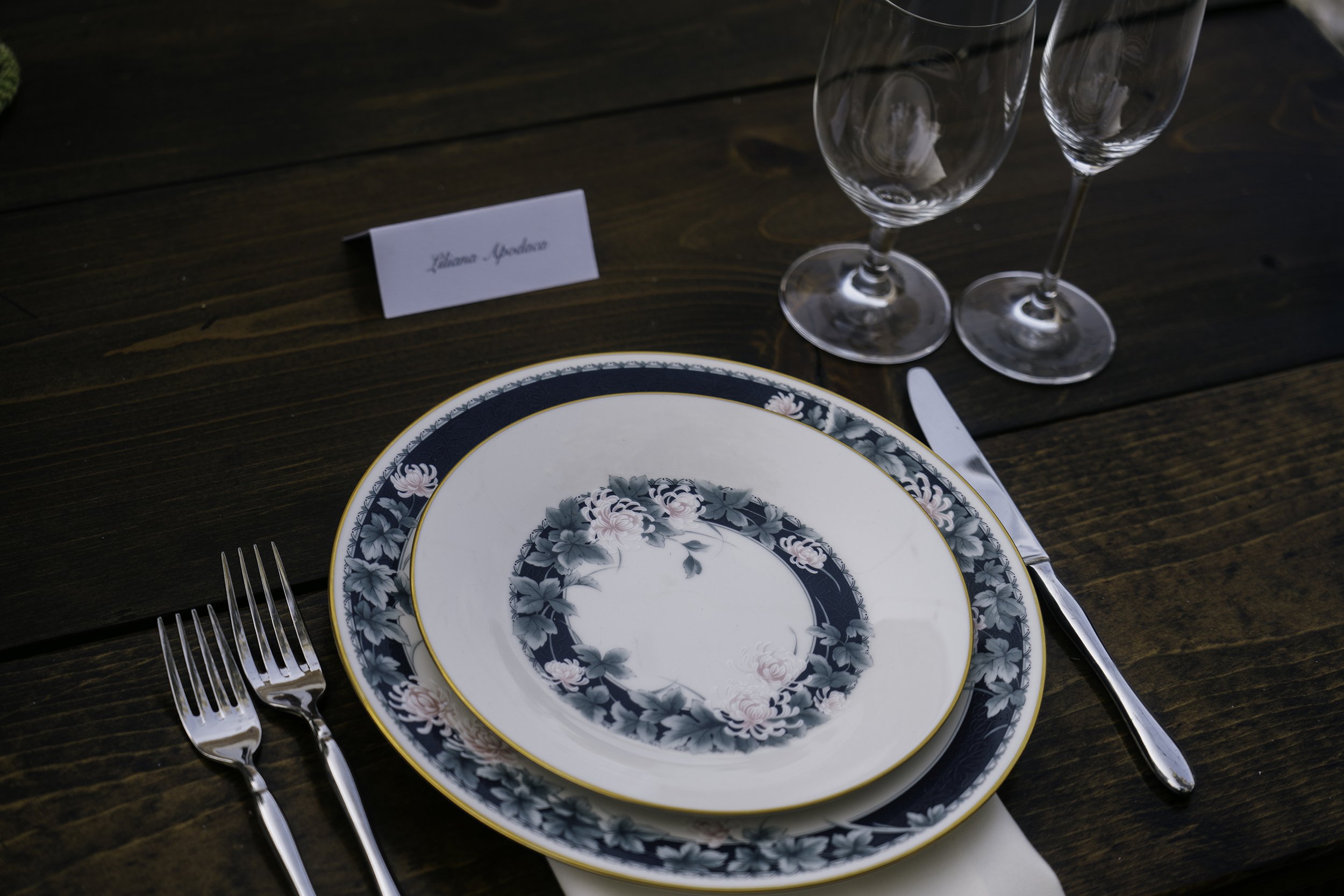 A place setting at a wedding featuring the floral Bouquet collection curated by Second Course Table, silverware, and glassware on a wooden table.