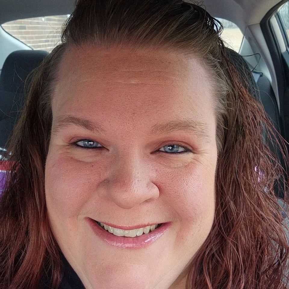 A woman with red hair smiling in a car.