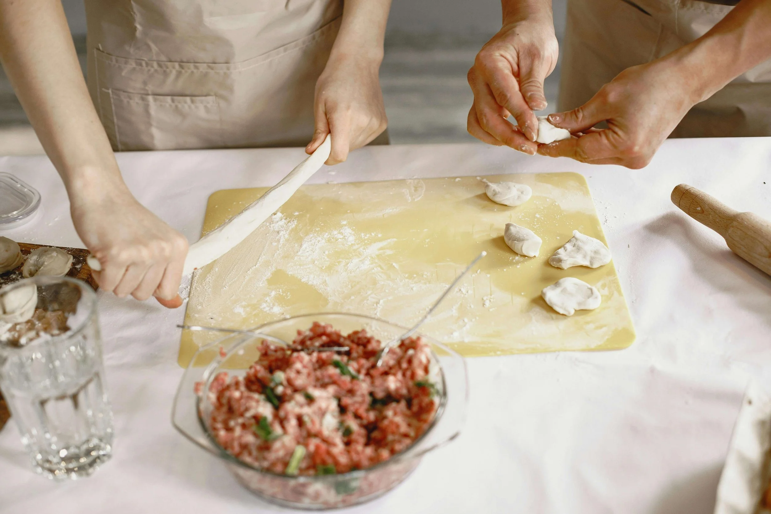 People making homemade dumplings with dough and meat filling on a floured surface.
