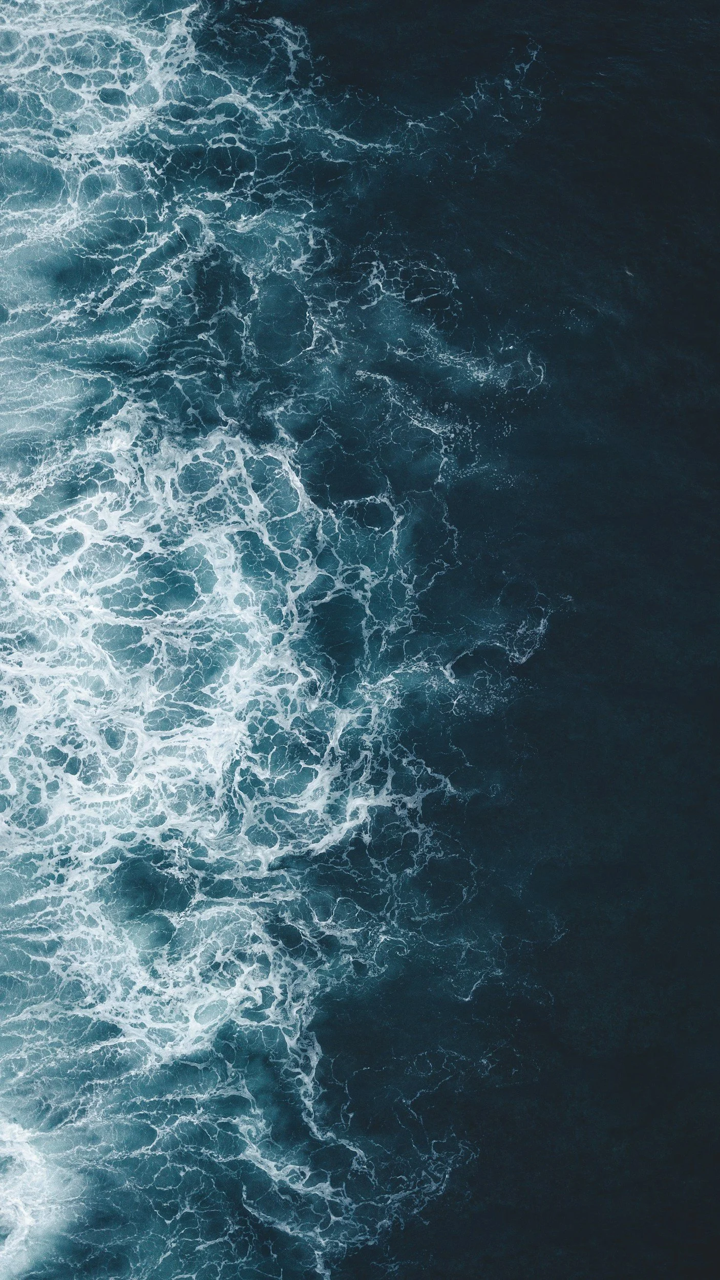 Aerial view of ocean waves with white foam on a deep blue sea.