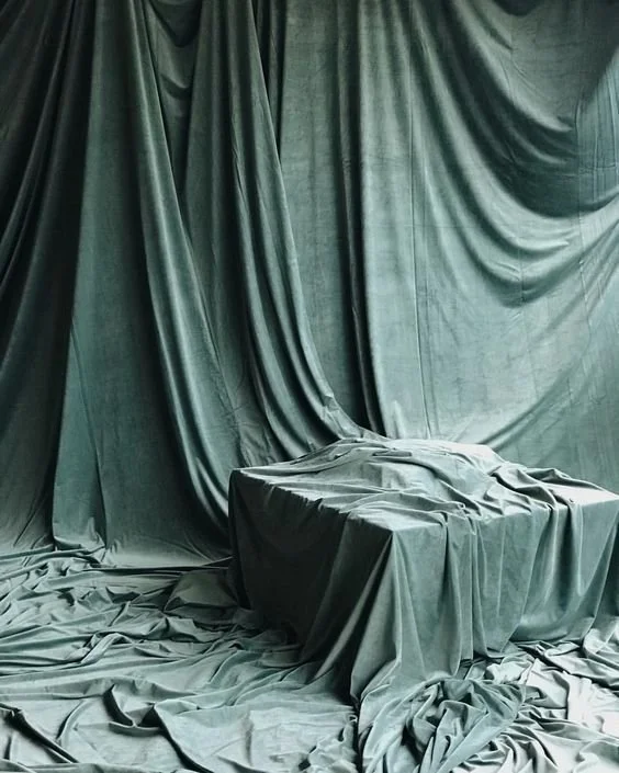 A chair covered with dark green fabric, surrounded by matching green drapes and fabric on the floor.