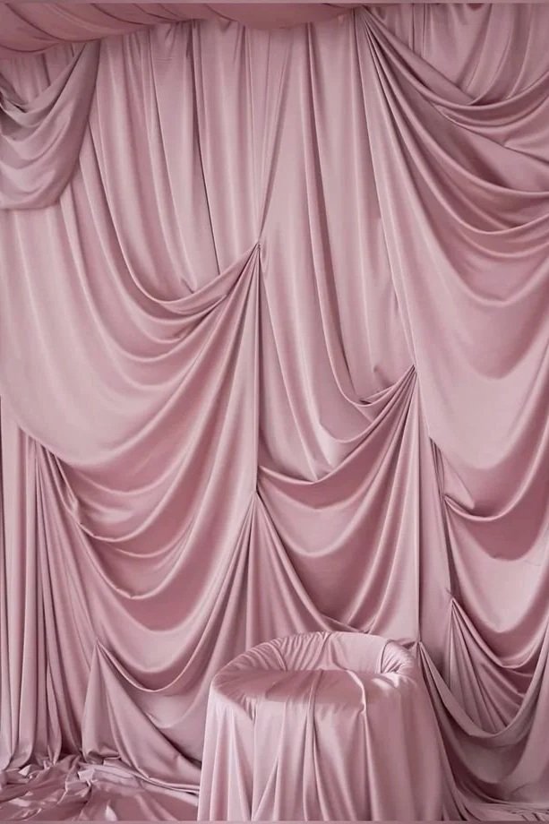 Pink satin curtain backdrop with gathered fabric and a satin-covered stool in front.