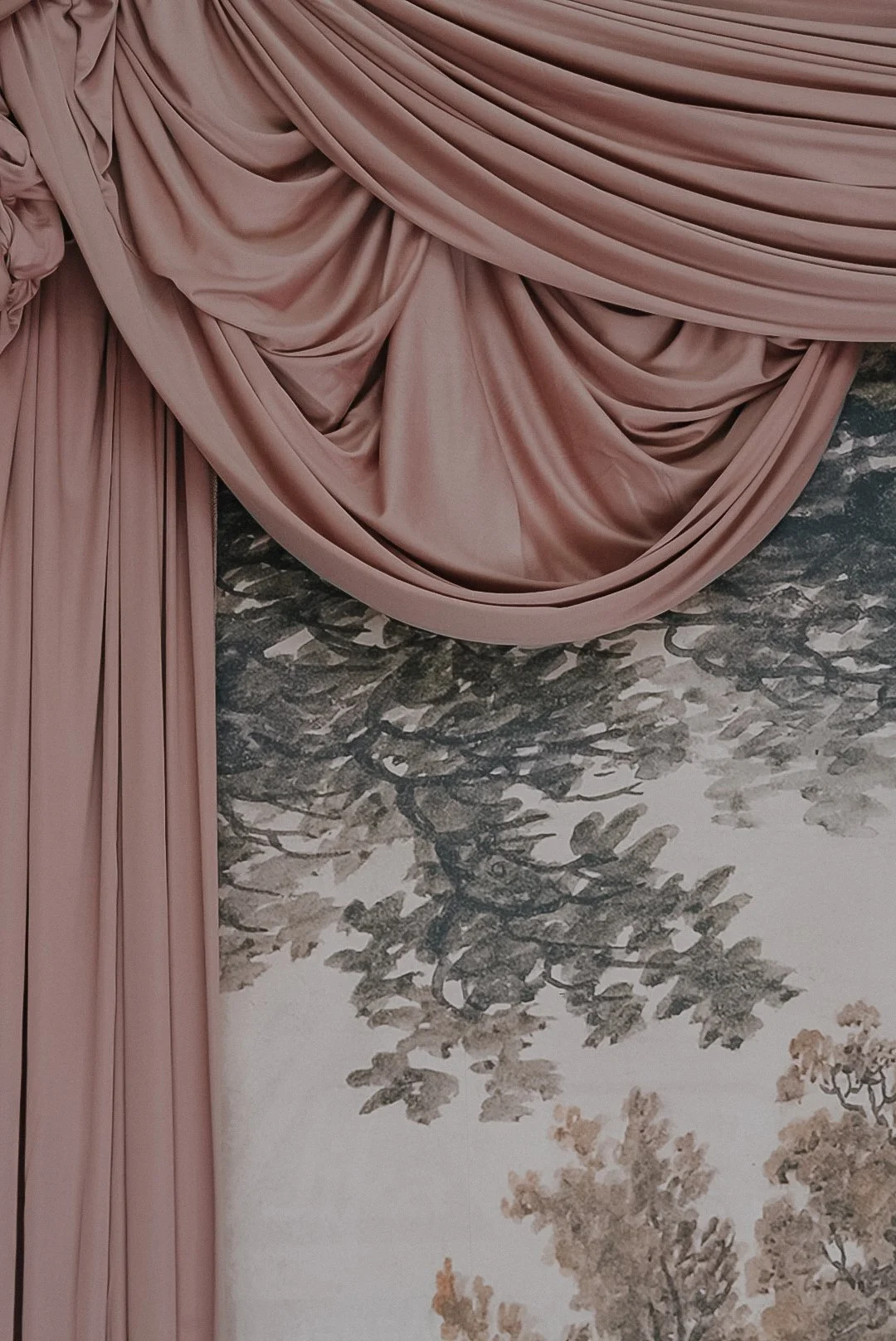 Pink draped fabric hanging above a painted mural of trees.