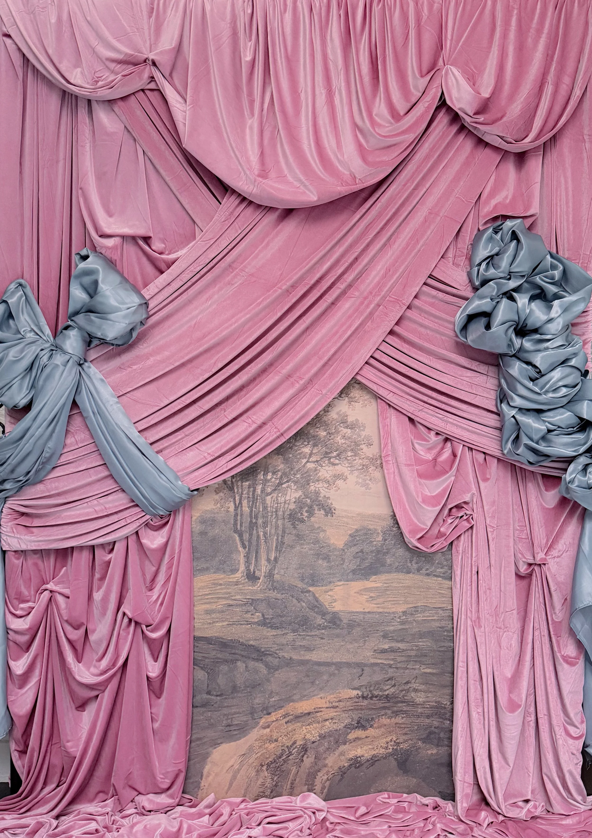 Pink velvet curtains draped around a painted mural wall with trees and a river