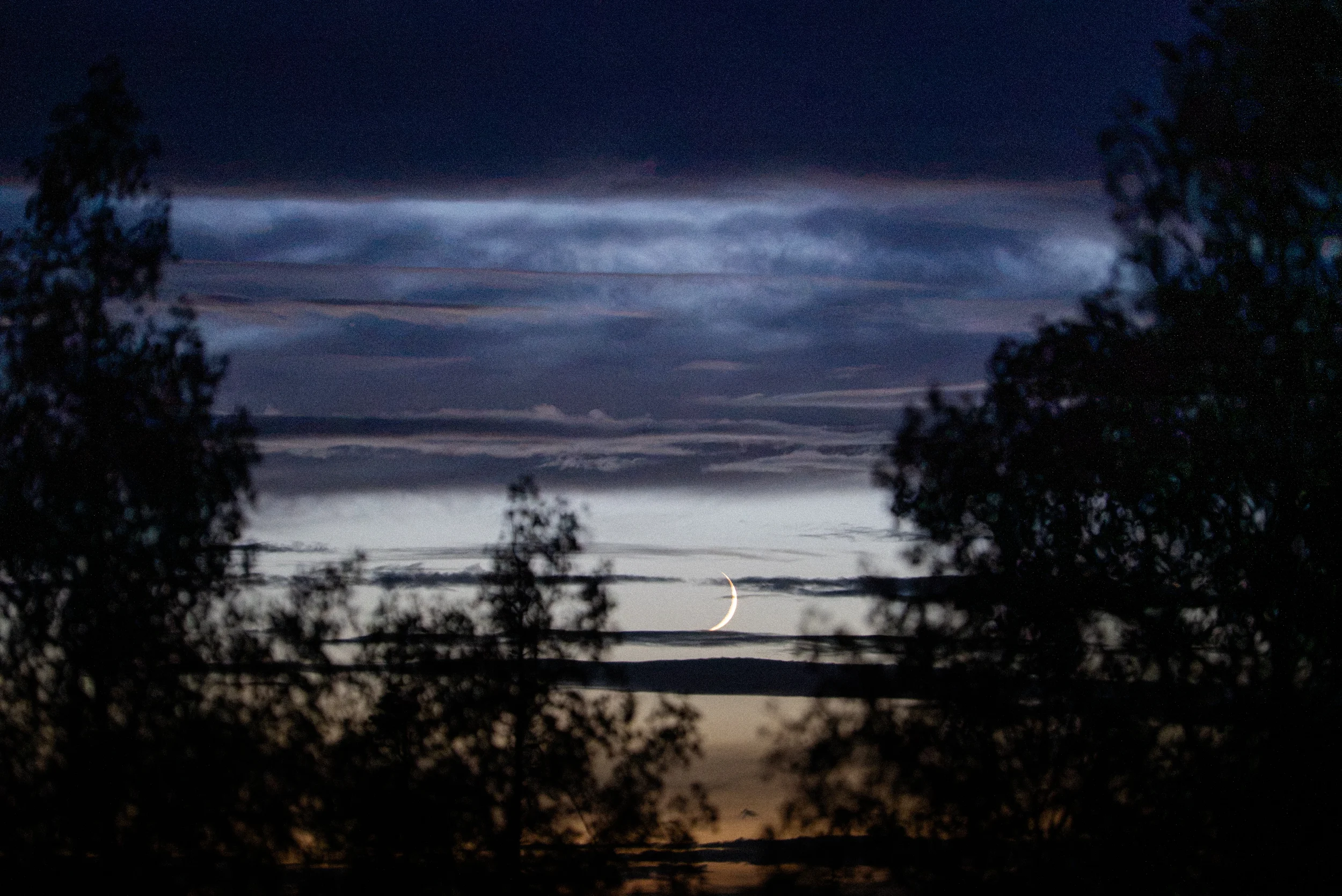 crescent moon poking through dark clouds