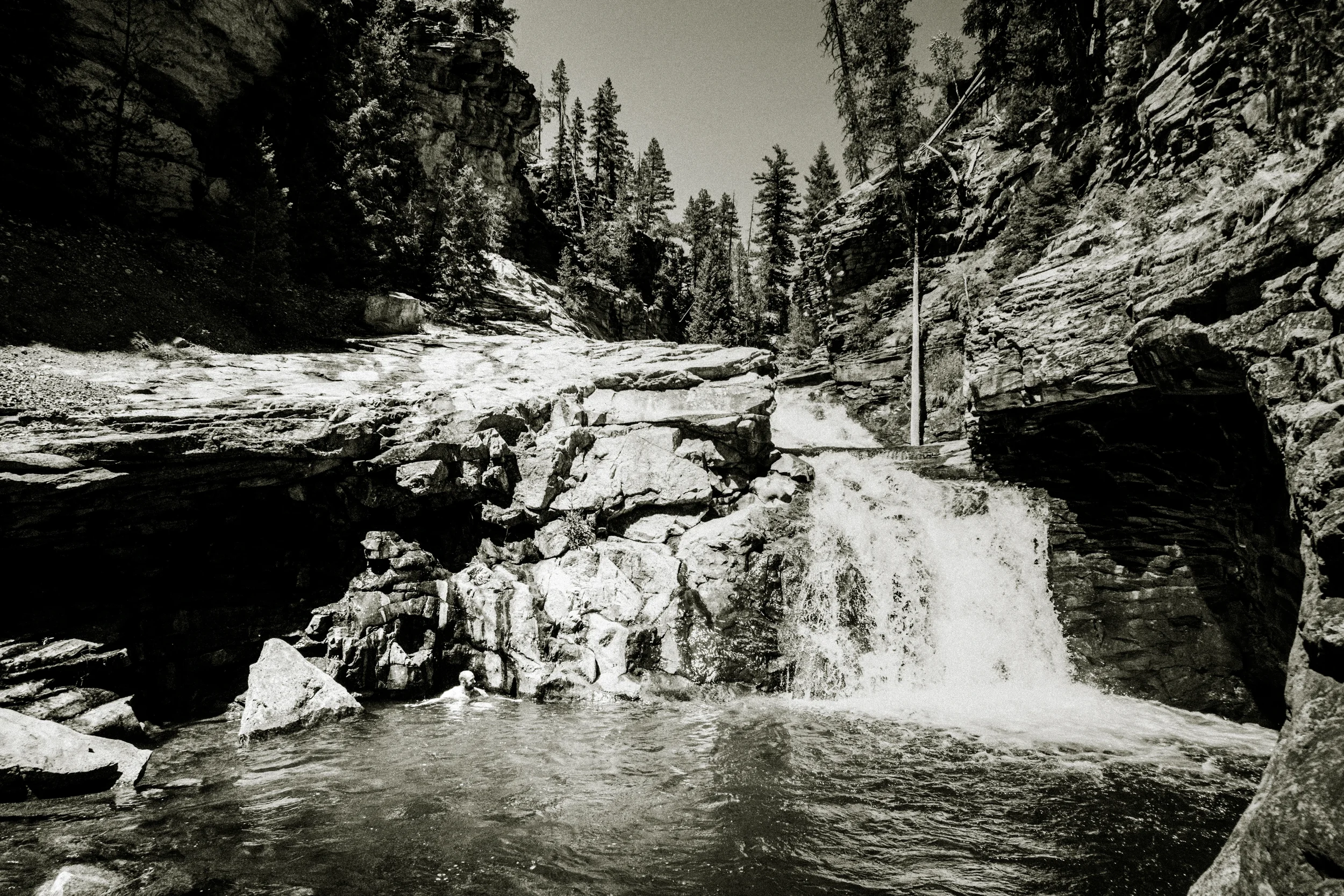 man swimming in a river near a waterfall