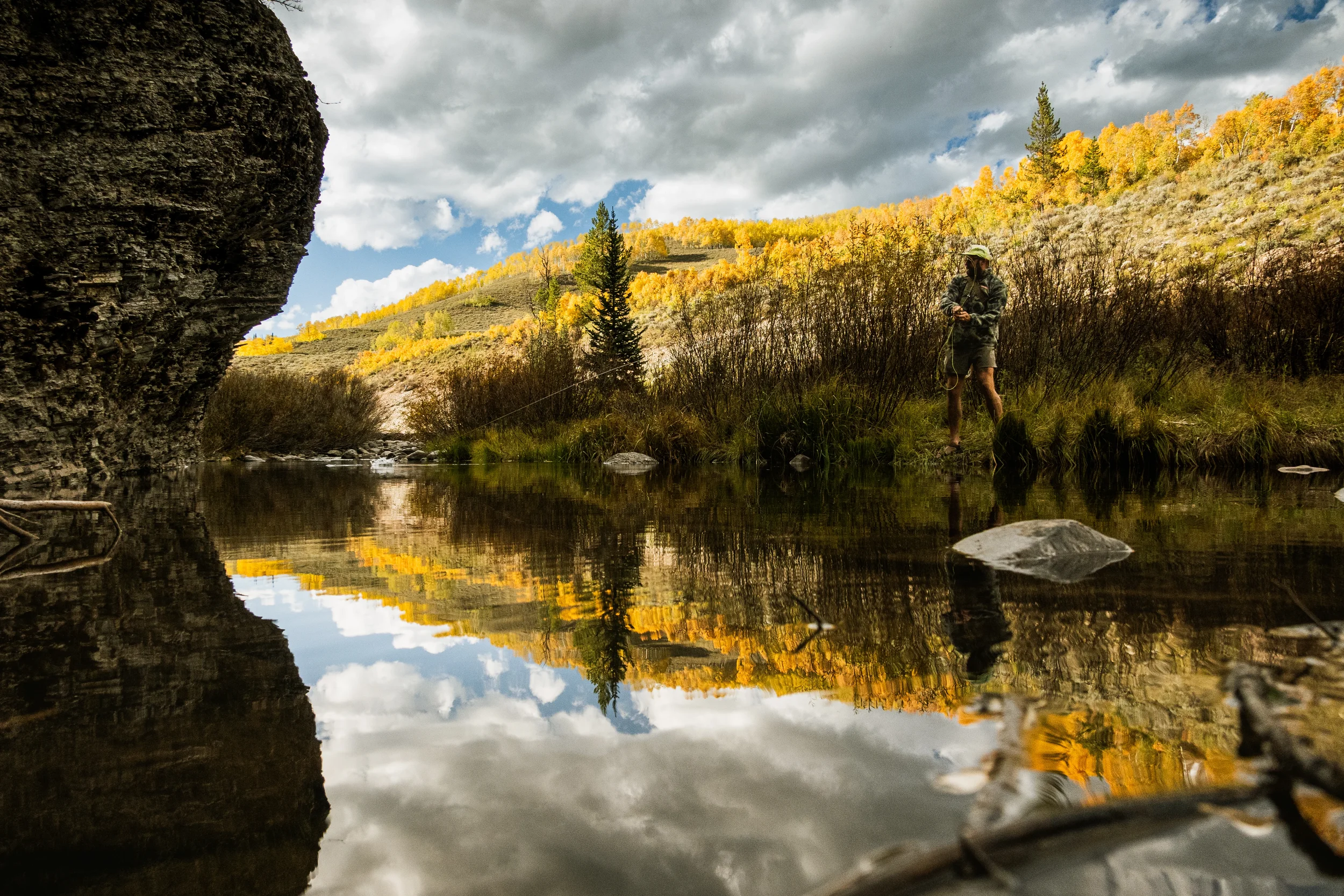 man fishing a small stream with fall colors