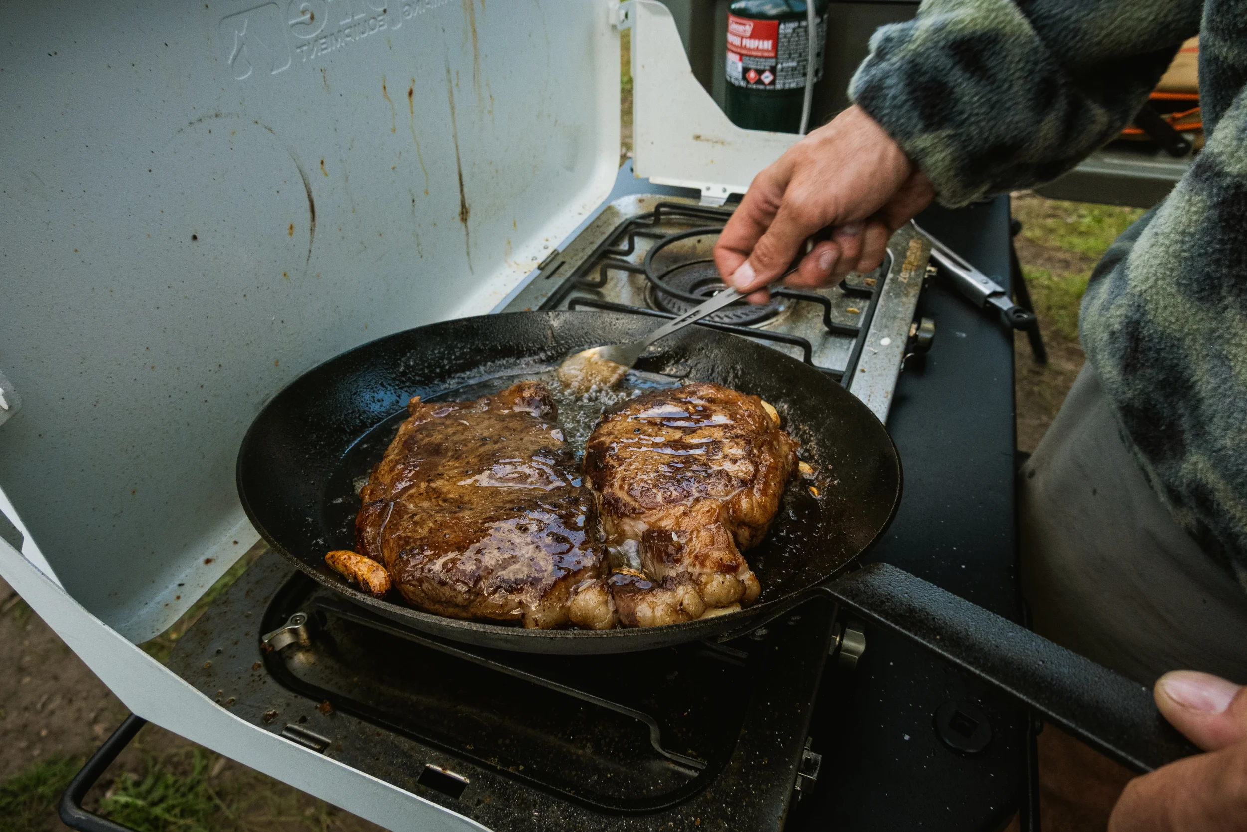 man butter basting steaks on a camp stove