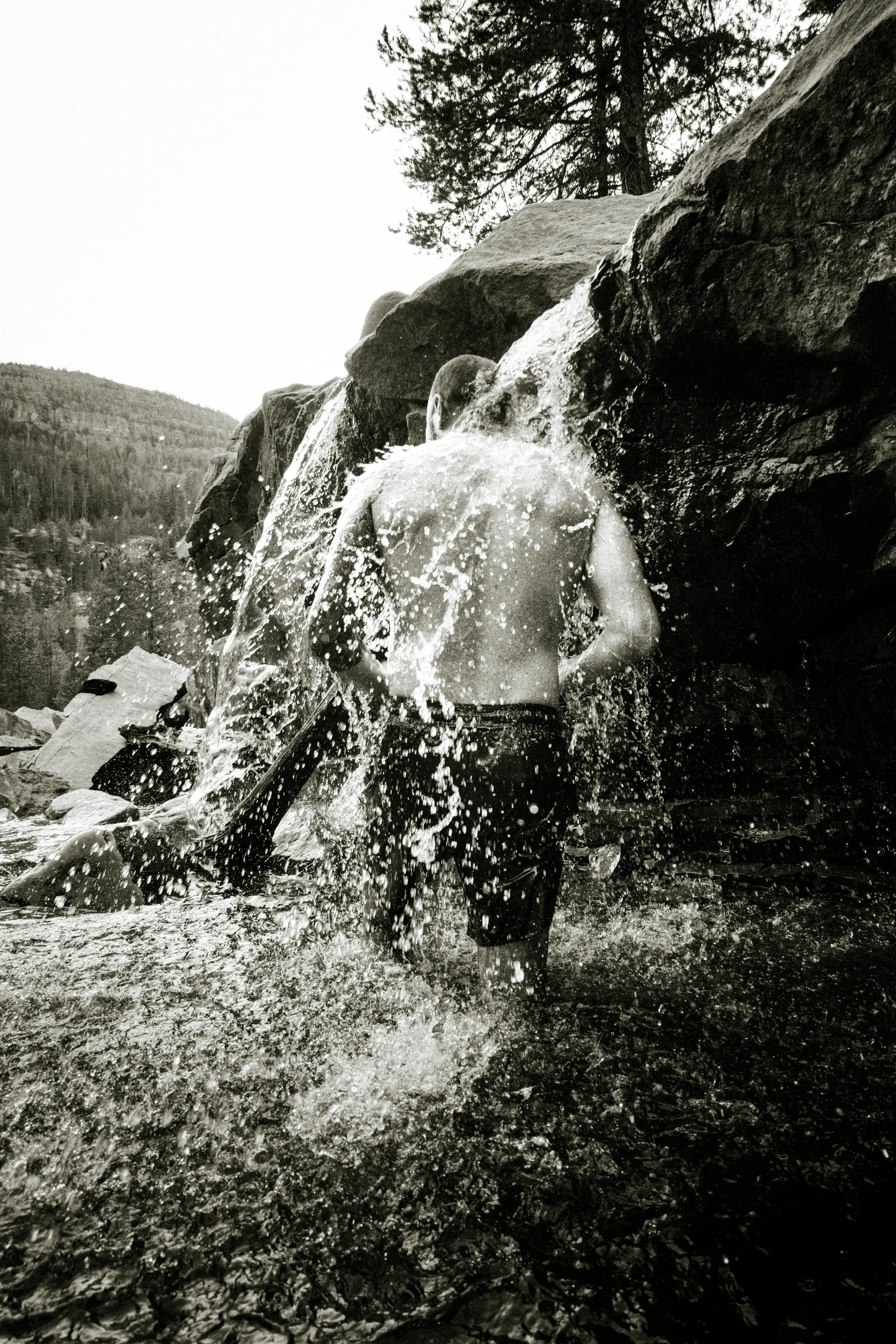man showering in a waterfall in a river