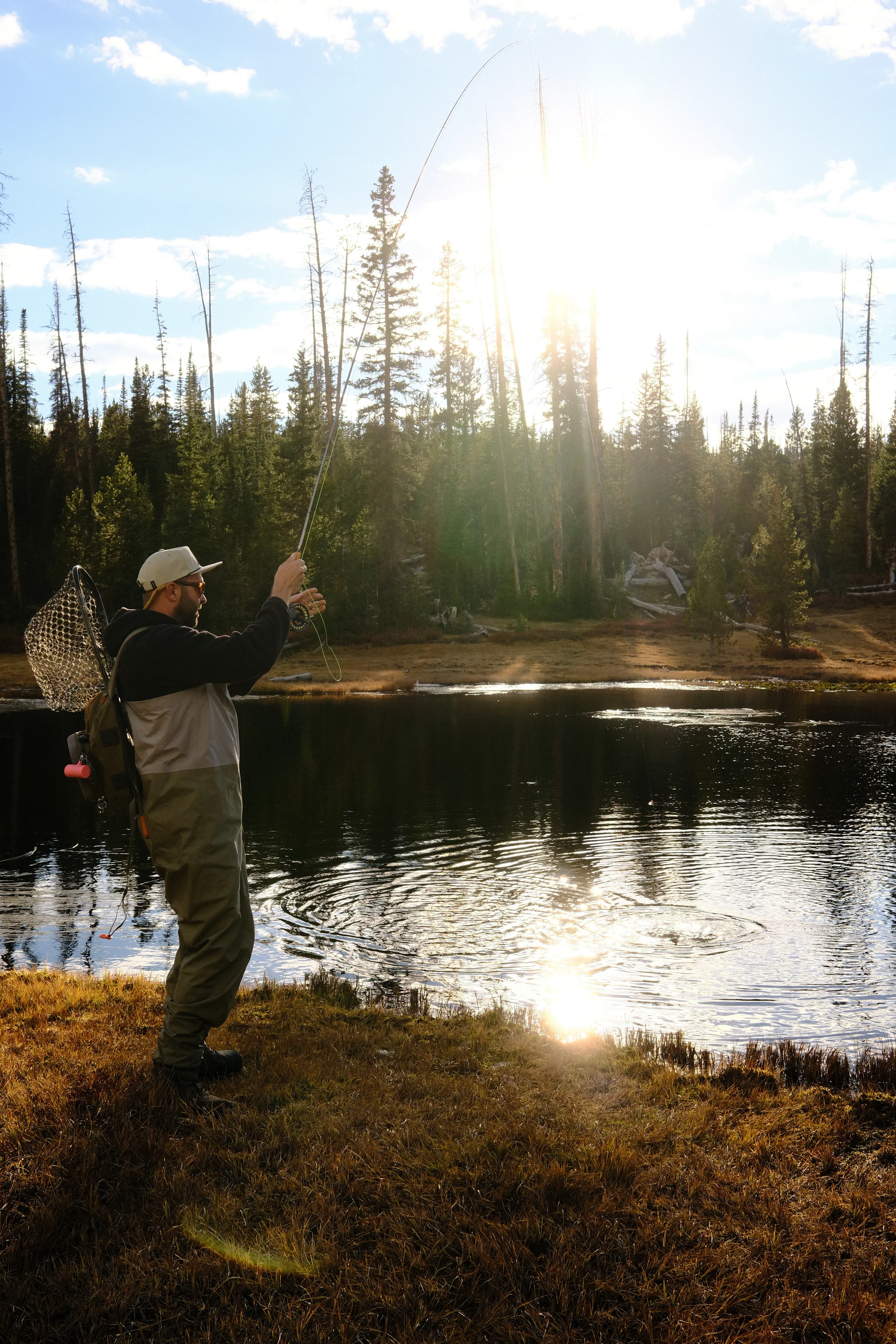 man reeling in a fish at the edge of a lake