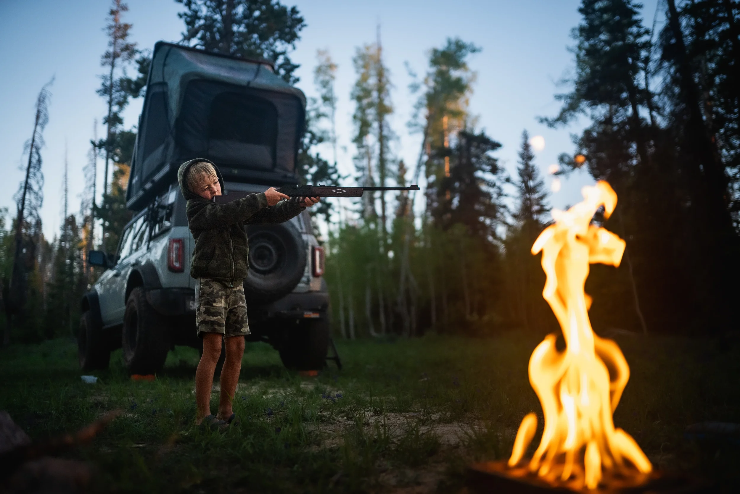 boy shooting a bb gun near a campfire