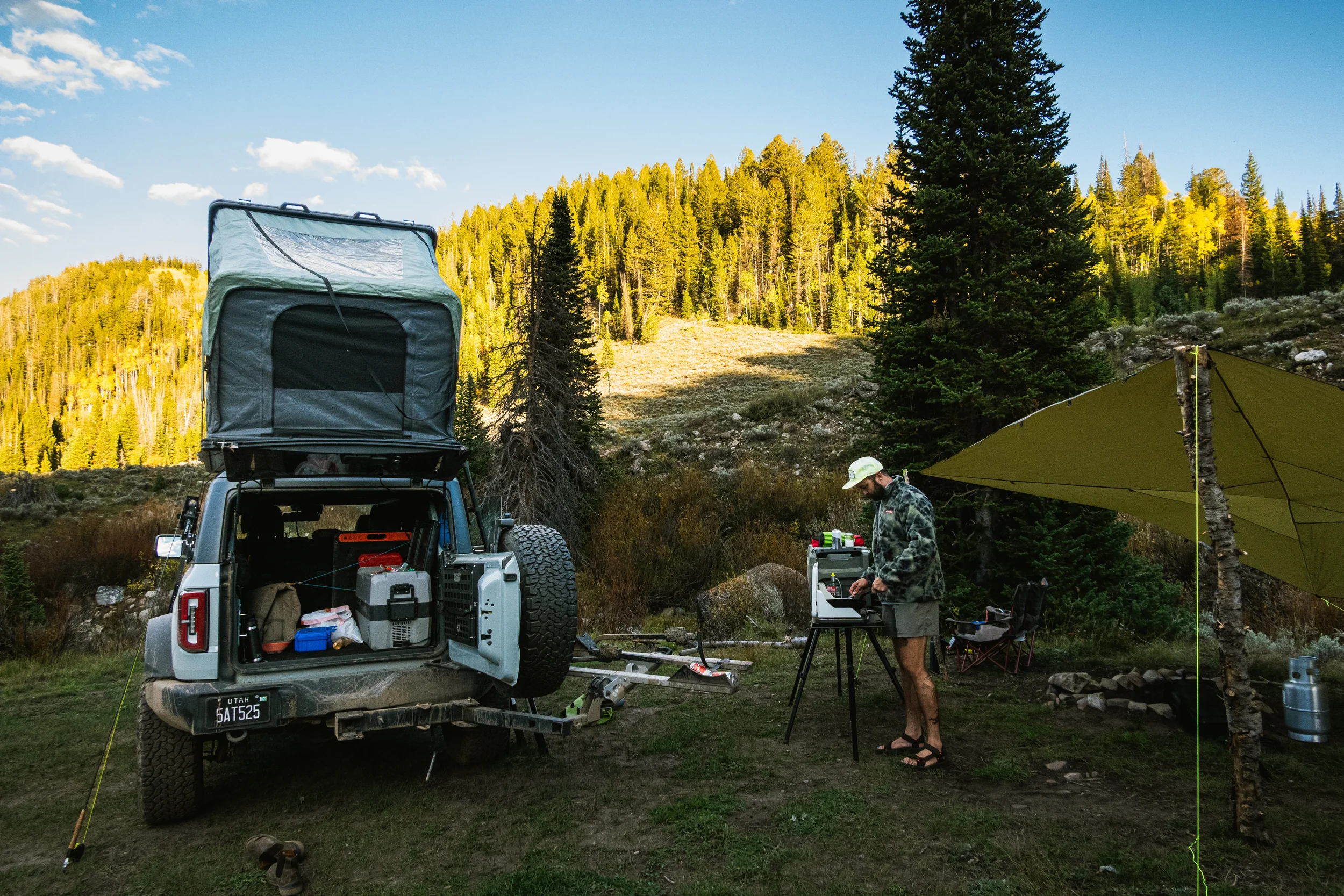 man cooking at a camp kitchen with a ford bronco nearby