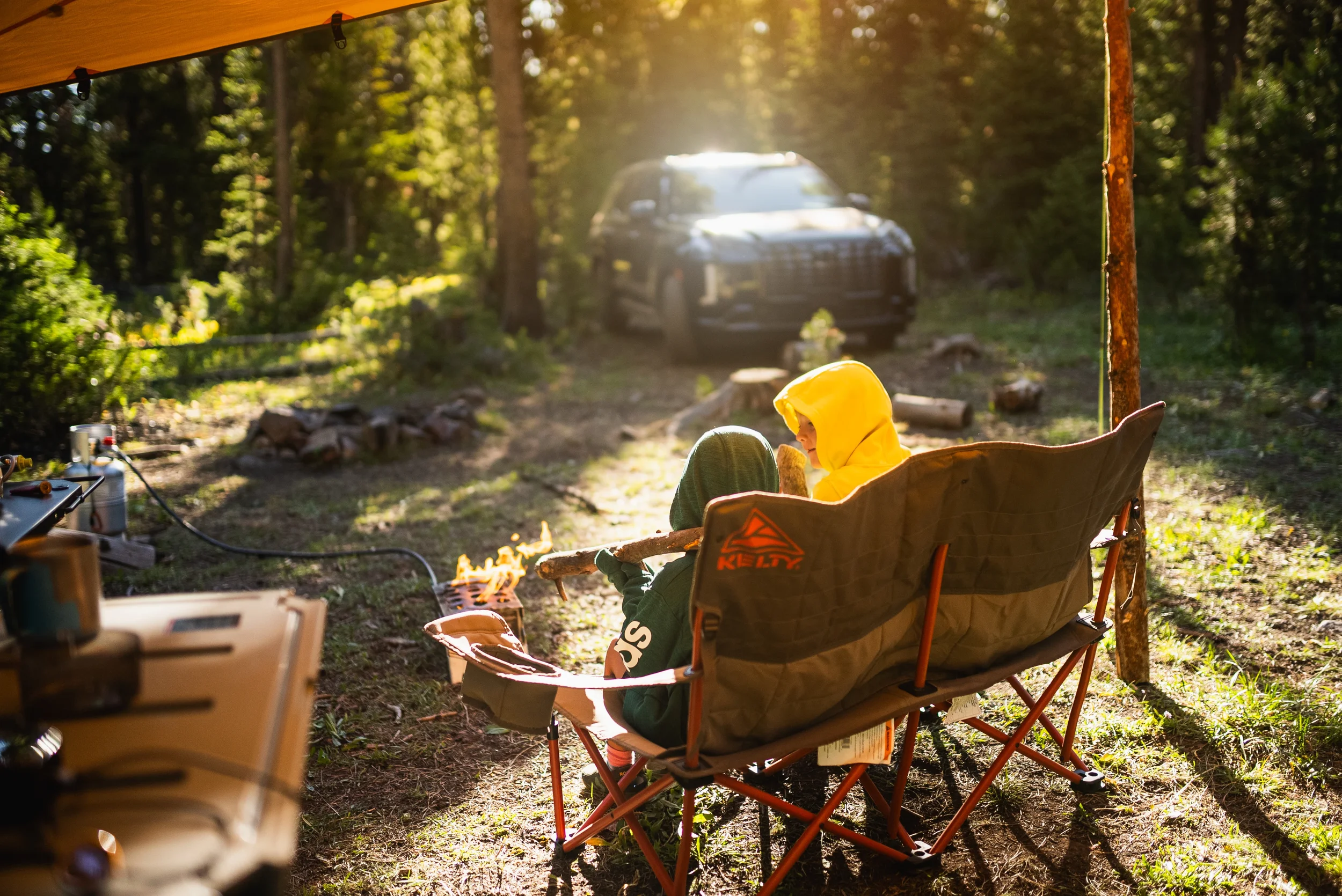 kids sitting in a camp chair near a fire