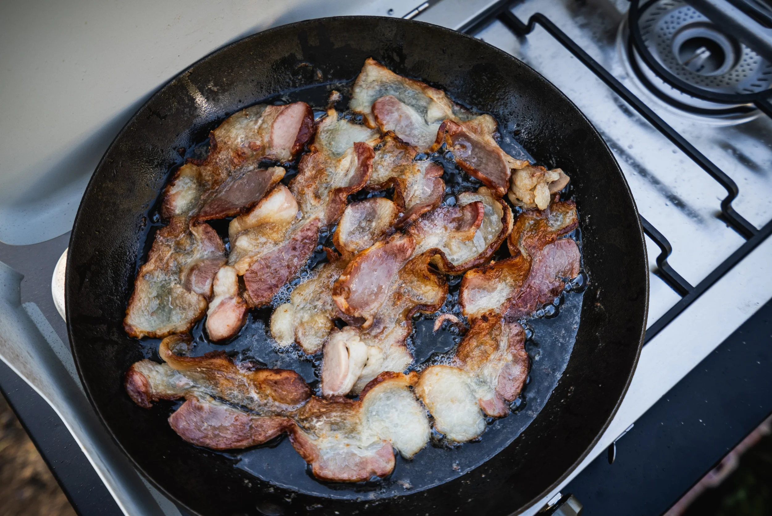 bacon frying in a pan on a camp stove
