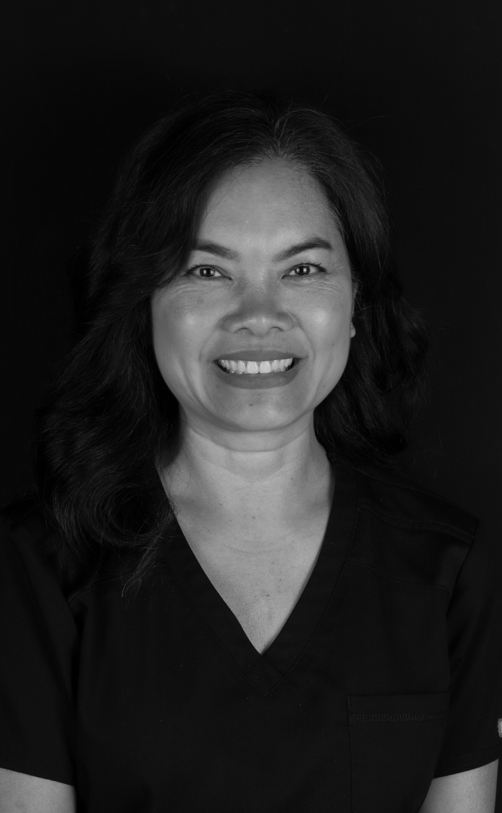 Black and white portrait of a woman with long, wavy hair, smiling, wearing a V-neck top, against a dark background.