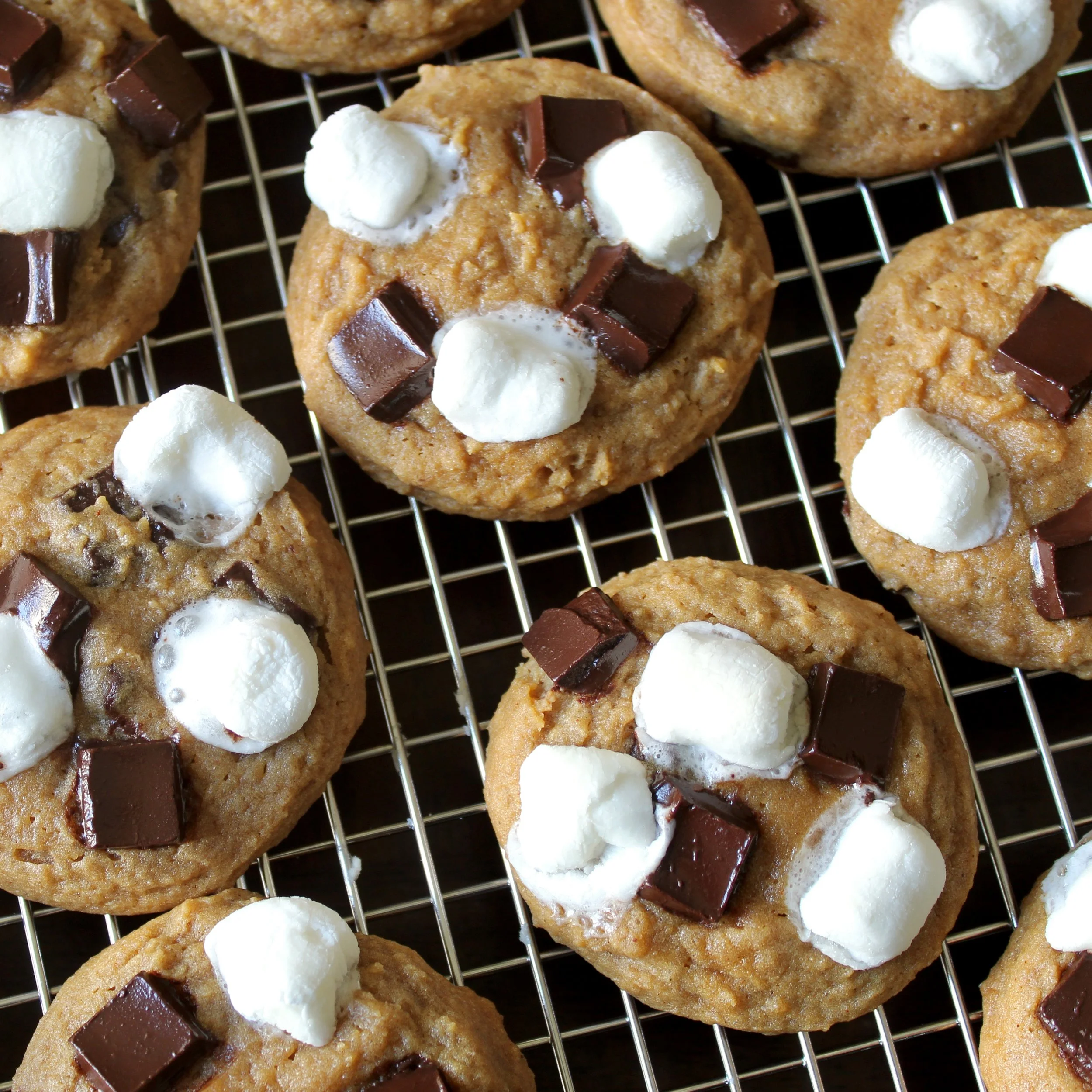 Freshly baked s'mores cookies loaded with melted chocolate chunks and soft marshmallows on a wire cooling rack.